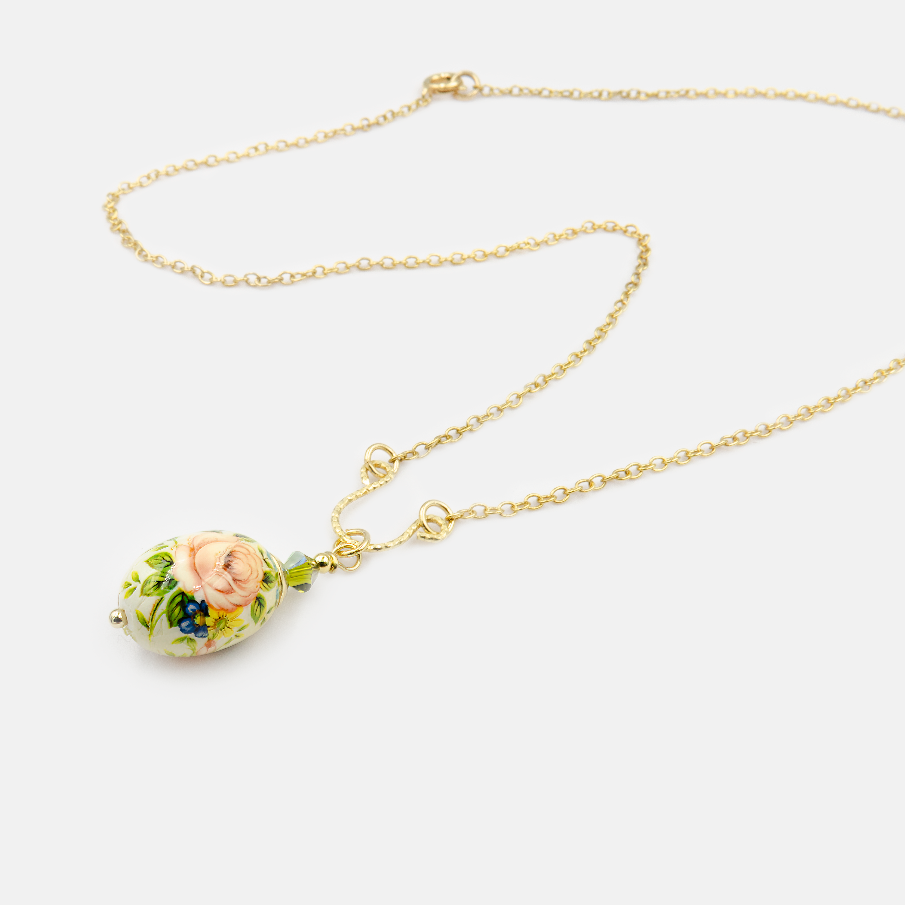 שרשרת קלאסית-רומנטית הכוללת תליון בצורת ביצה קטנה, עשוי חרסינה או זכוכית בגימור מבריק, עם ציור פרחוני צבעוני בסגנון עתיק. שיבוץ חרוזים ירוקים בחיבור מוסיף נגיעה טבעית, ומחבר בין רכות לצבע.