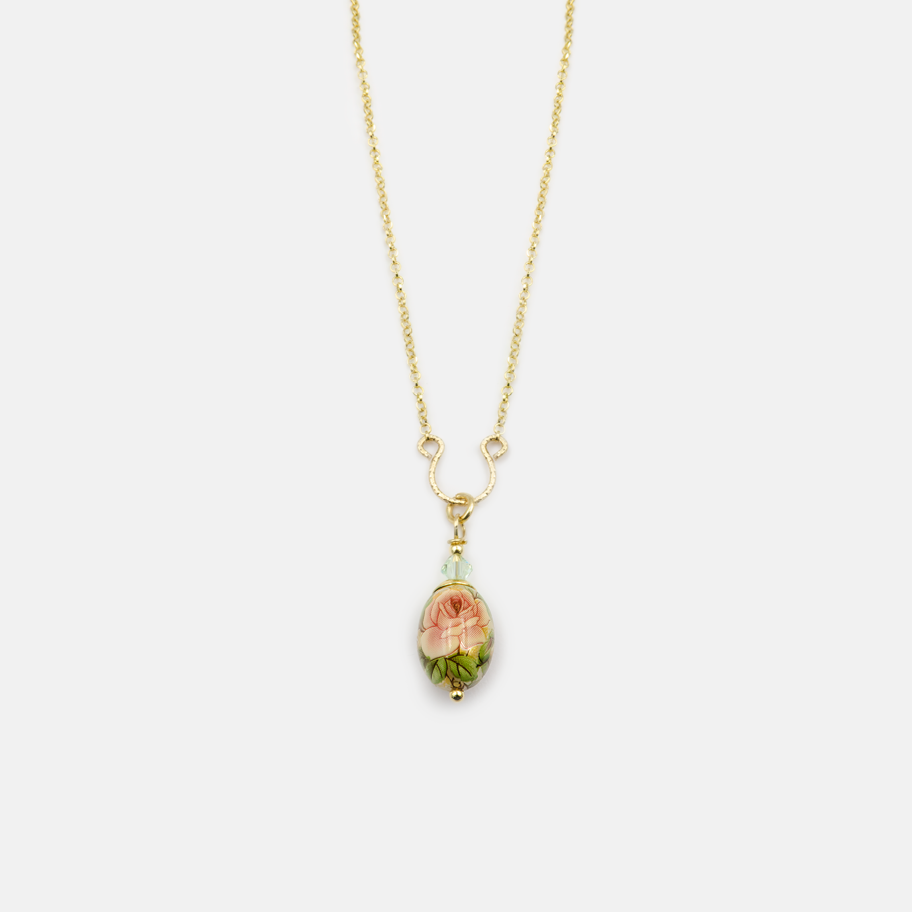 שרשרת מוזהבת עם תליון בצורת ביצה מעוטרת בעבודת יד בגווני ירוק. התליון כולל ציור פרחוני בגווני ירוק פסטלי עם עלים בגווני זית ויער, ופרטים קטנים בכחול כהה. חיבור התליון משולב בחרוזי זכוכית ירוקים. עיצוב נשי, טבעי ורך, עם תחושת רוגע ואלגנטיות.