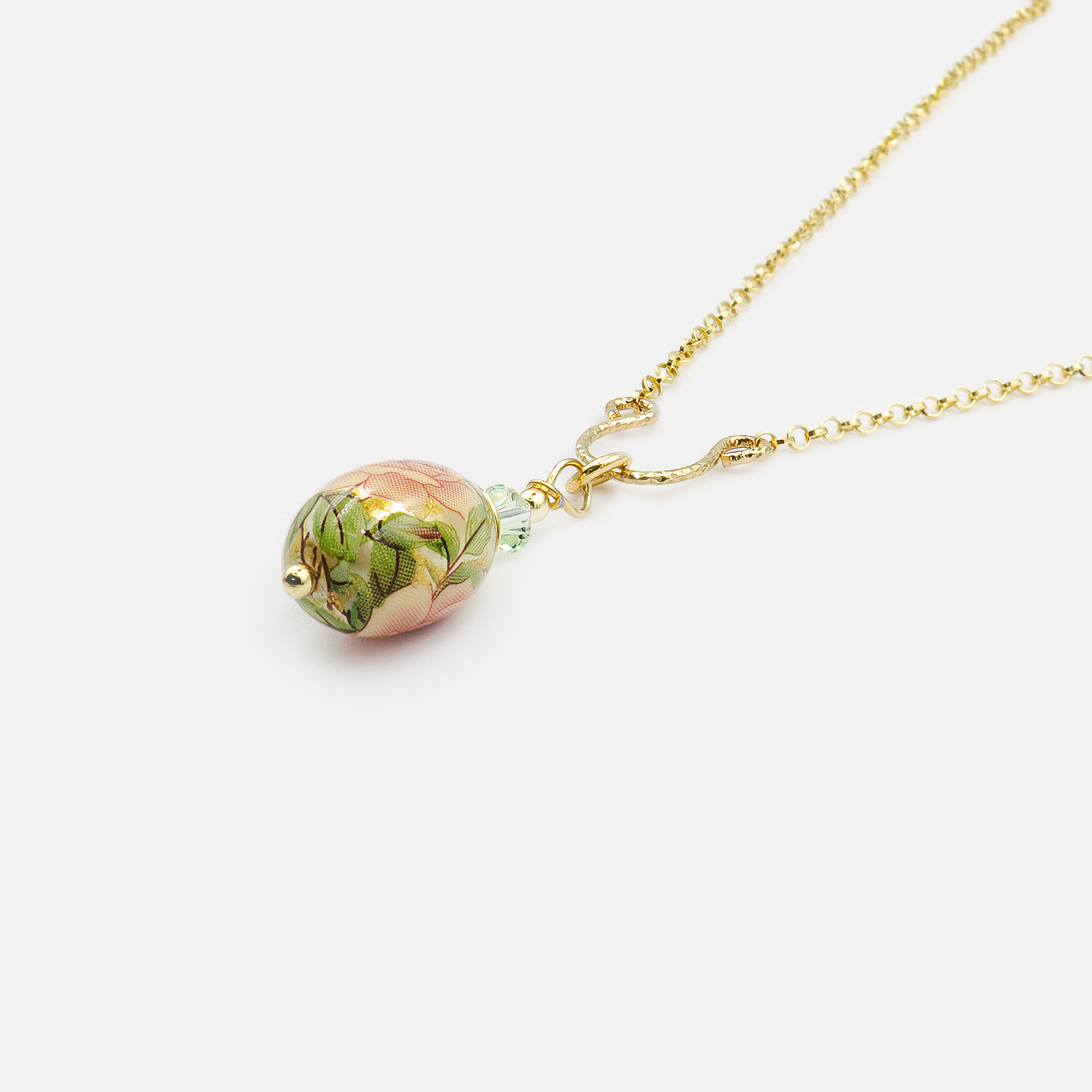שרשרת בסגנון רומנטי עם תליון קרמי אובלי, מעוטר בפרח בגוון ירוק מרווה רך, מוקף בציורי עלים ירוקים ופרחים כחולים קטנים. חיבור עם חרוזים ירוקים מנצנצים. עיצוב קלאסי עם ניחוח נוסטלגי – מושלם לאוהבות תכשיטים בהשראת טבע.