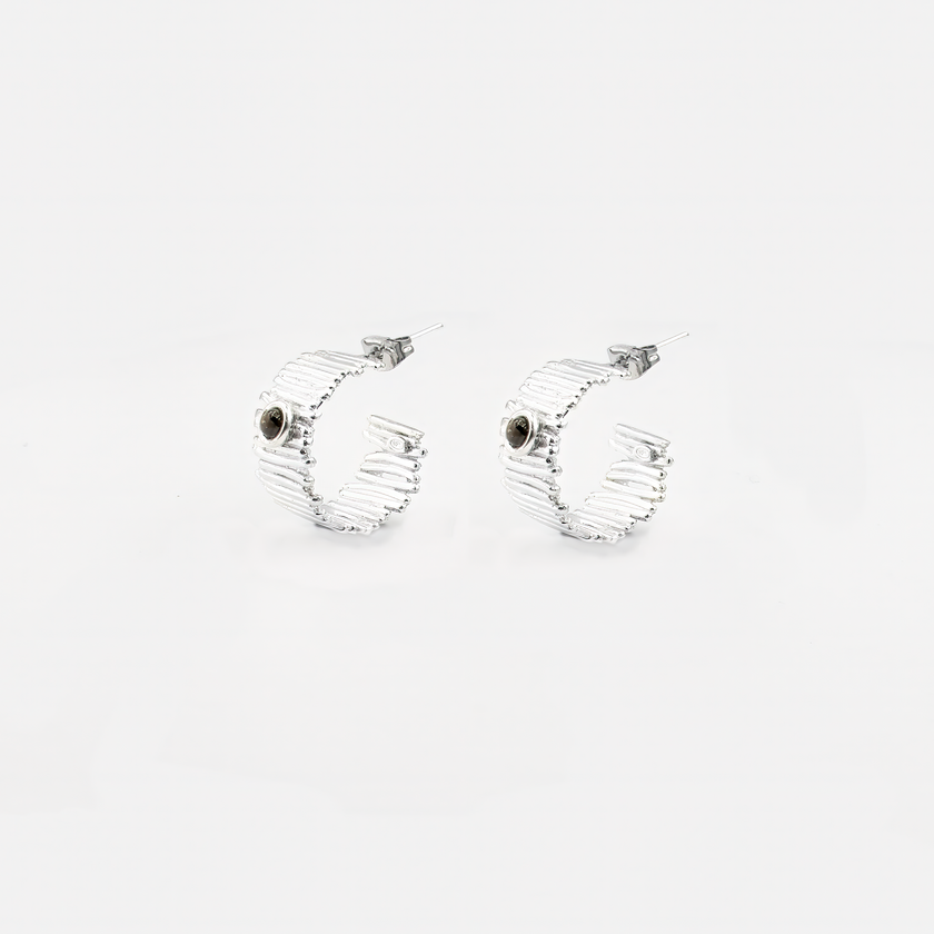 עגילי חישוק בעבודת יד מכסף 925, משובצים סמוקי טופז בגוון חום מעושן – תכשיט בעל אופי מיוחד, שמתאים לנשים שמחפשות סטייל עם עומק. האבן יוצרת מראה אלגנטי עם טוויסט מחוספס אך עדין, כזה שמשתלב נהדר עם כל צבע עור וביגוד ניטרלי או כהה. החישוק הקליל והמדויק מעניק תנועה נעימה ותחושת זרימה, בעוד האבן מוסיפה נוכחות שקטה. תכשיט מושלם כמתנה ייחודית ליום הולדת, לאירוע חשוב או לעצמך – כתזכורת לעוצמה פנימית ולחיבור אל הקרקע.

