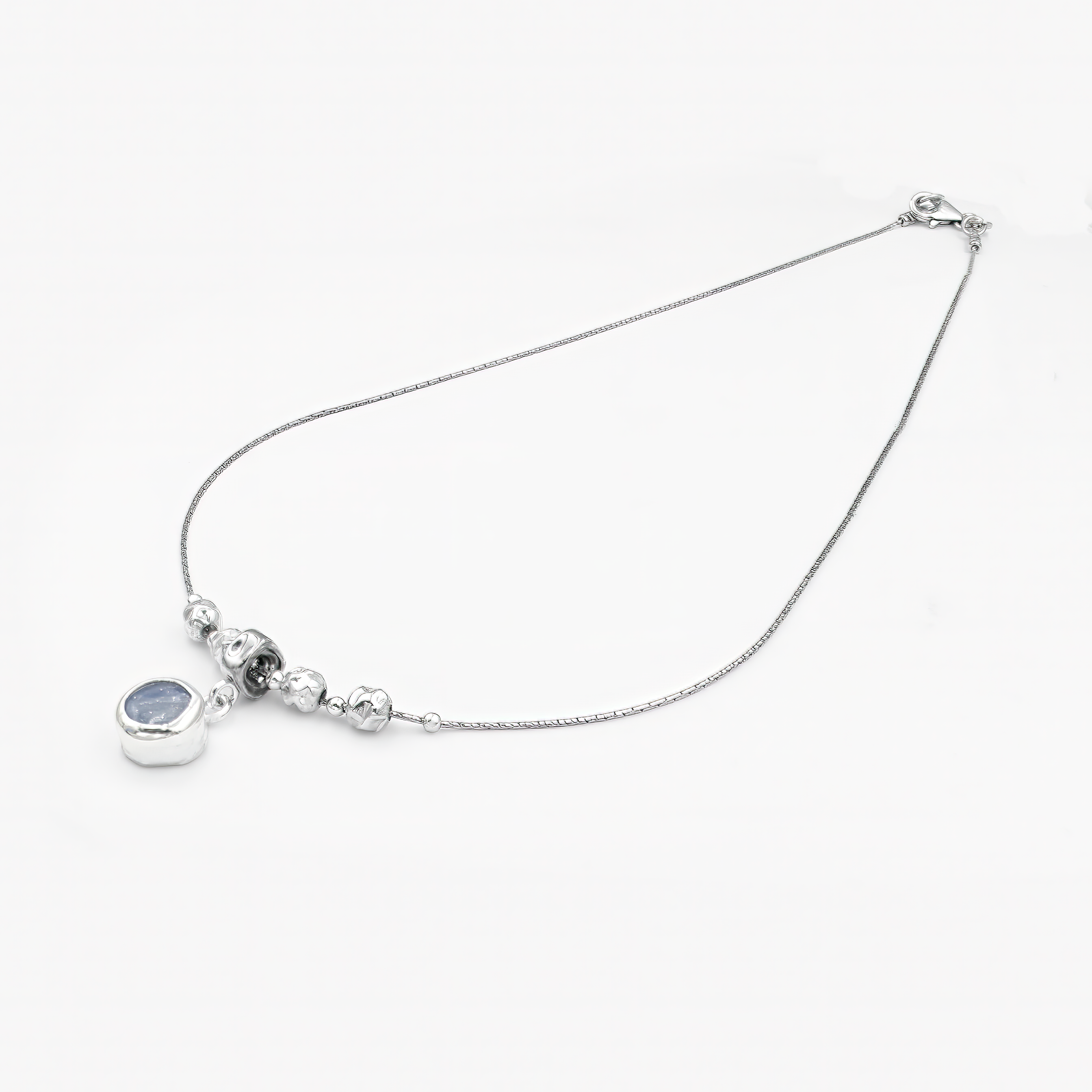 שרשרת אלגנטית בעיצוב מינימליסטי ומעודן, עשויה כסף מבריק עם שרשרת דקה ועדינה. במרכז השרשרת שורת חרוזים כסופים מעוגלים, היוצרים איזון סימטרי, ומתחתיהם תלוי תליון עגול קטן המשובץ באבן חן כחולה בגוון שמיים-עמוק. האבן בעלת מרקם טבעי ופנימי משתנה, מה שמוסיף לתכשיט נוכחות רגועה אך בולטת. מתאים למראה יומיומי עם טאץ' אלגנטי או כלוק ערב שקט ומעודן.