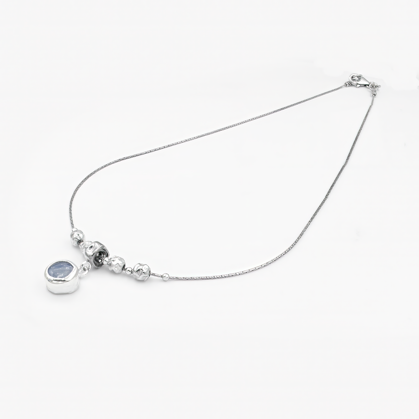 שרשרת אלגנטית בעיצוב מינימליסטי ומעודן, עשויה כסף מבריק עם שרשרת דקה ועדינה. במרכז השרשרת שורת חרוזים כסופים מעוגלים, היוצרים איזון סימטרי, ומתחתיהם תלוי תליון עגול קטן המשובץ באבן חן כחולה בגוון שמיים-עמוק. האבן בעלת מרקם טבעי ופנימי משתנה, מה שמוסיף לתכשיט נוכחות רגועה אך בולטת. מתאים למראה יומיומי עם טאץ' אלגנטי או כלוק ערב שקט ומעודן.