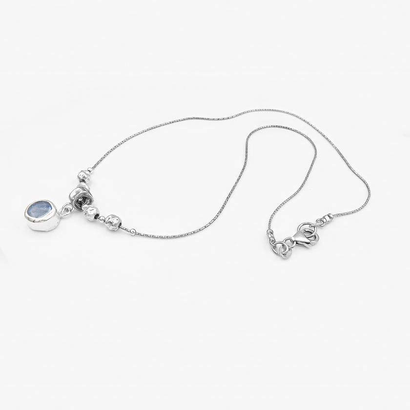 שרשרת מכסף סטרלינג בגימור מבריק, בעלת מרכז דקורטיבי הכולל חמישה חרוזים כסופים עגולים. תליון קטן ועגול משתלשל מתחת לחרוז המרכזי ומשובץ באבן כחולה בגוון קריסטלי-טבעי. האבן מזכירה את הגוון של קיאניט או ספיר לייט ומוסיפה אלמנט של עומק וצבע קריר. התליון במסגרת סגורה וקווים נקיים משתלב בצורה מושלמת עם שאר התכשיט, ומשדר איזון בין תחכום לפשטות.

