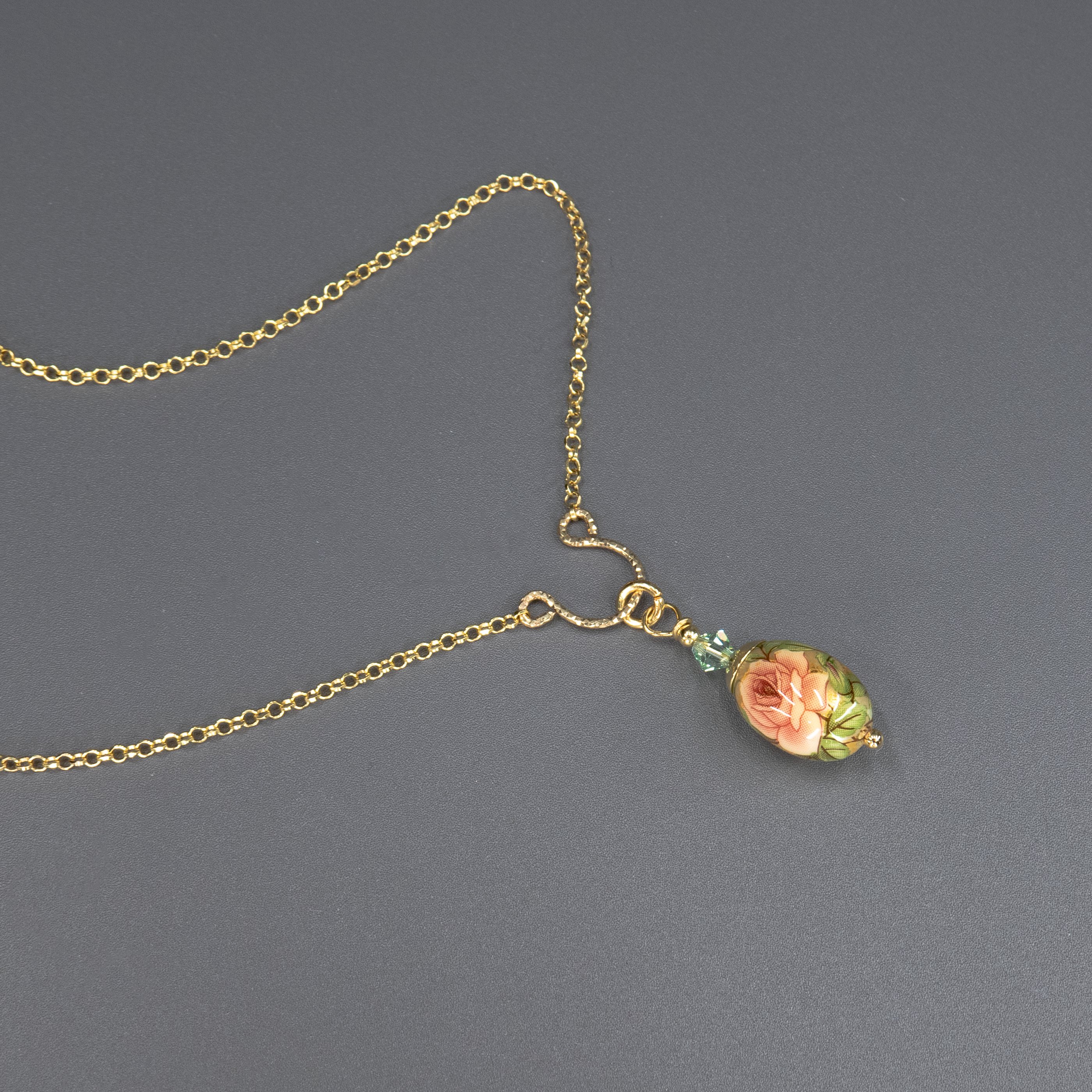 שרשרת אלגנטית בעיצוב וינטג' עם תליון קרמי אובלי בגוון ירקרק, מצויר ביד עם פרח רך בגווני ירוק בהיר, מוקף עלים כהים ופרחים זעירים. החרוזים המחברים בולטים בגוון ירוק אזמרגד מבריק. תכשיט שמזכיר יער אביבי וטבע רגוע.
