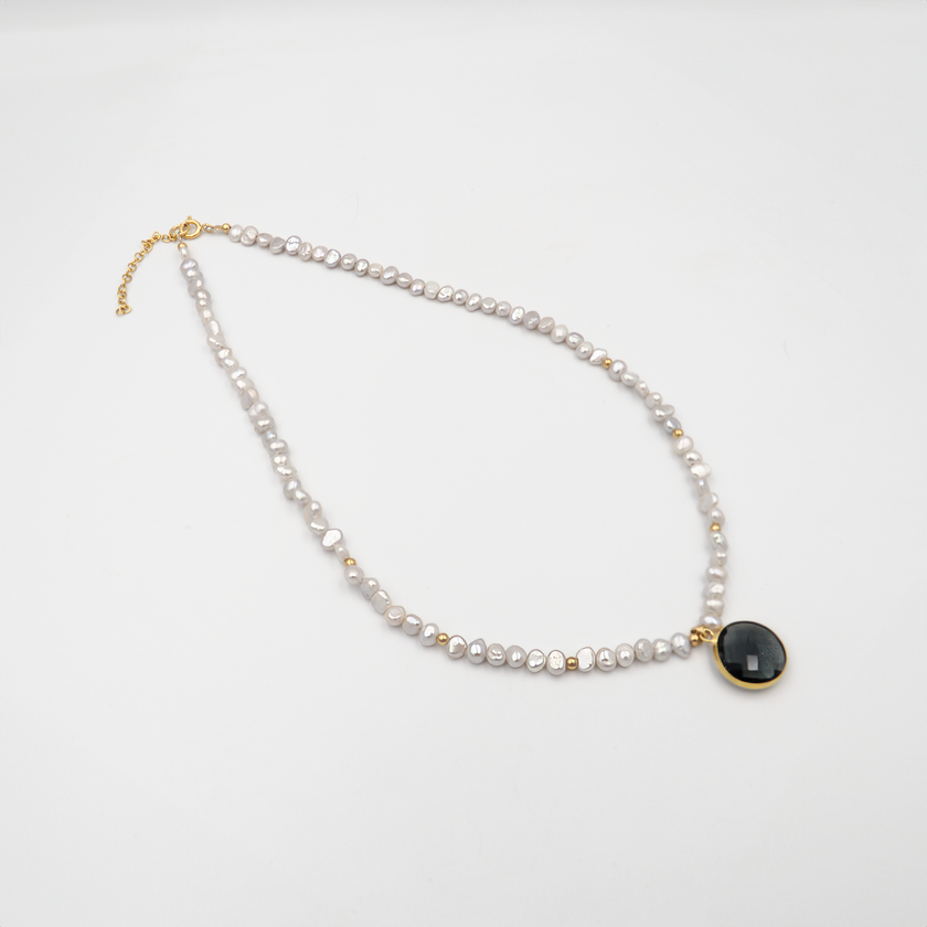 שרשרת אלגנטית עם פניני לבנדר עם תליון מרכזי – תכשיט בעלת מראה רך ויוקרתי. הפנינים סגלגלות ובעלות ברק פנינתי טבעי, מעניקות לשרשרת אווירה חלומית ונשית. התליון משתלב בצורה הרמונית עם רצף הפנינים, מוסיף נקודת מוקד עיצובית ומאזן בין פשטות לרושם. מתאימה לענידה ביום יום וגם לאירועים מיוחדים – מושלם למי שמחפשת צבע לא שגרתי באלגנטיות.