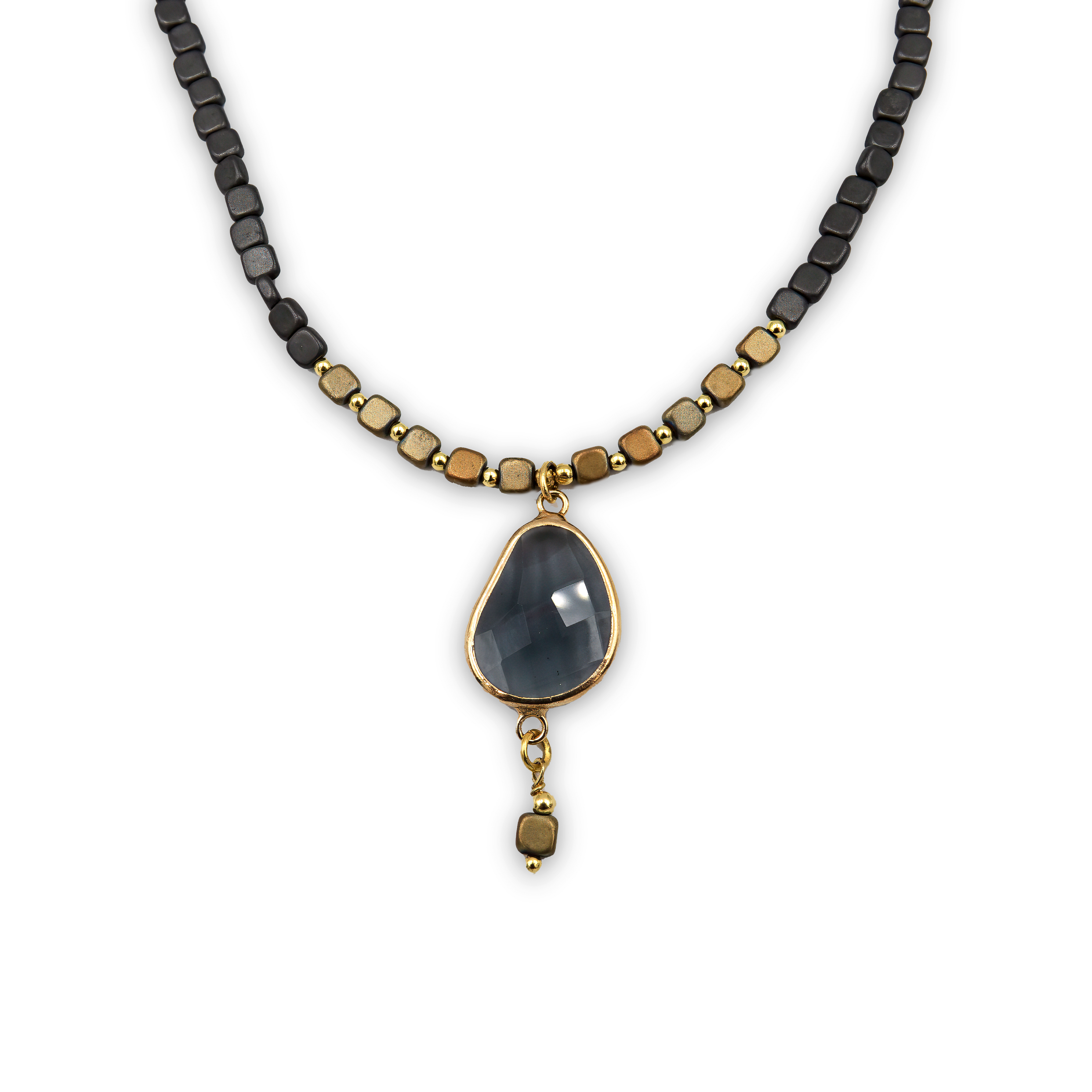 שרשרת בעבודת יד שמשלבת אלגנטיות עם עיצוב גיאומטרי מודרני. החלק המרכזי כולל תליון טיפה גדול עשוי אבן בגוון אפור כהה עם ליטוש פנים עדין, משובץ במסגרת מתכת מוזהבת. מהתליון משתלשל חרוז מרובע קטן שמעניק תנועה ונופך אקזוטי. השרשרת עצמה מורכבת מחרוזים מרובעים בגוונים משתנים של שחור, זהב, ונחושת מטאליים, לסירוגין. שילוב בין גוונים כהים ומוזהבים יוצר מראה דרמטי, מושלם ללבוש ערב או כהצהרת אופנה ייחודית.