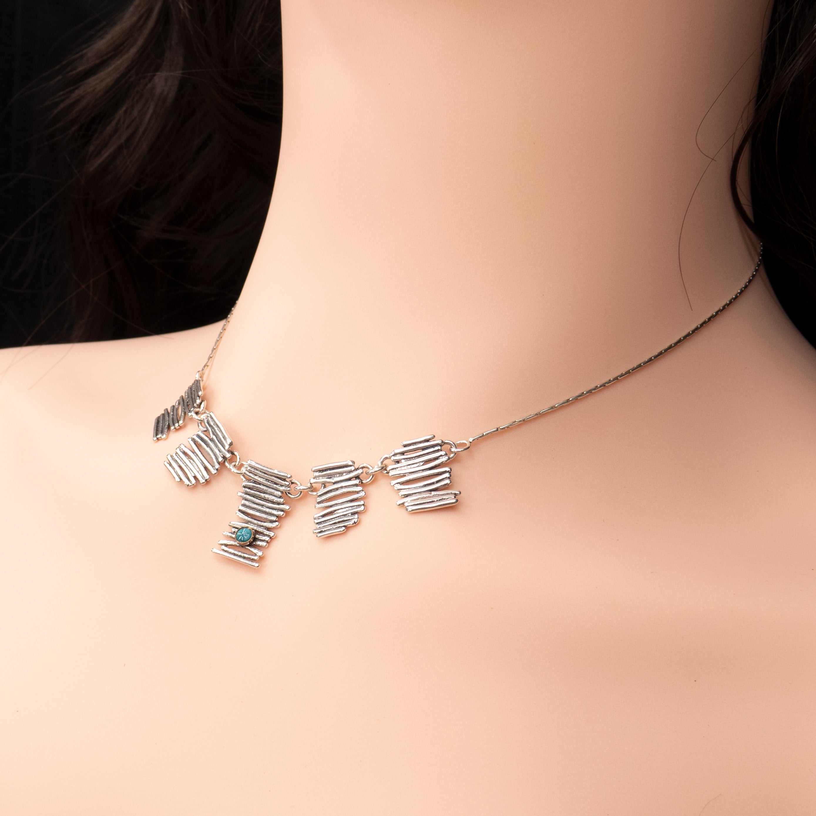 שרשרת כסף מעוצבת עם שלוש יחידות מרקם מופשטות המדמות קווים חופשיים. בכל יחידה שובצה אבן טורקיז טבעית – בחיתוכים שונים – בגוון כחול רך ומרגיע. העיצוב נקי אך עשיר בפרטים, משדר איזון בין מודרנה לאותנטיות. מתאימה למראה יומיומי עם נגיעה של צבע ונשמה.