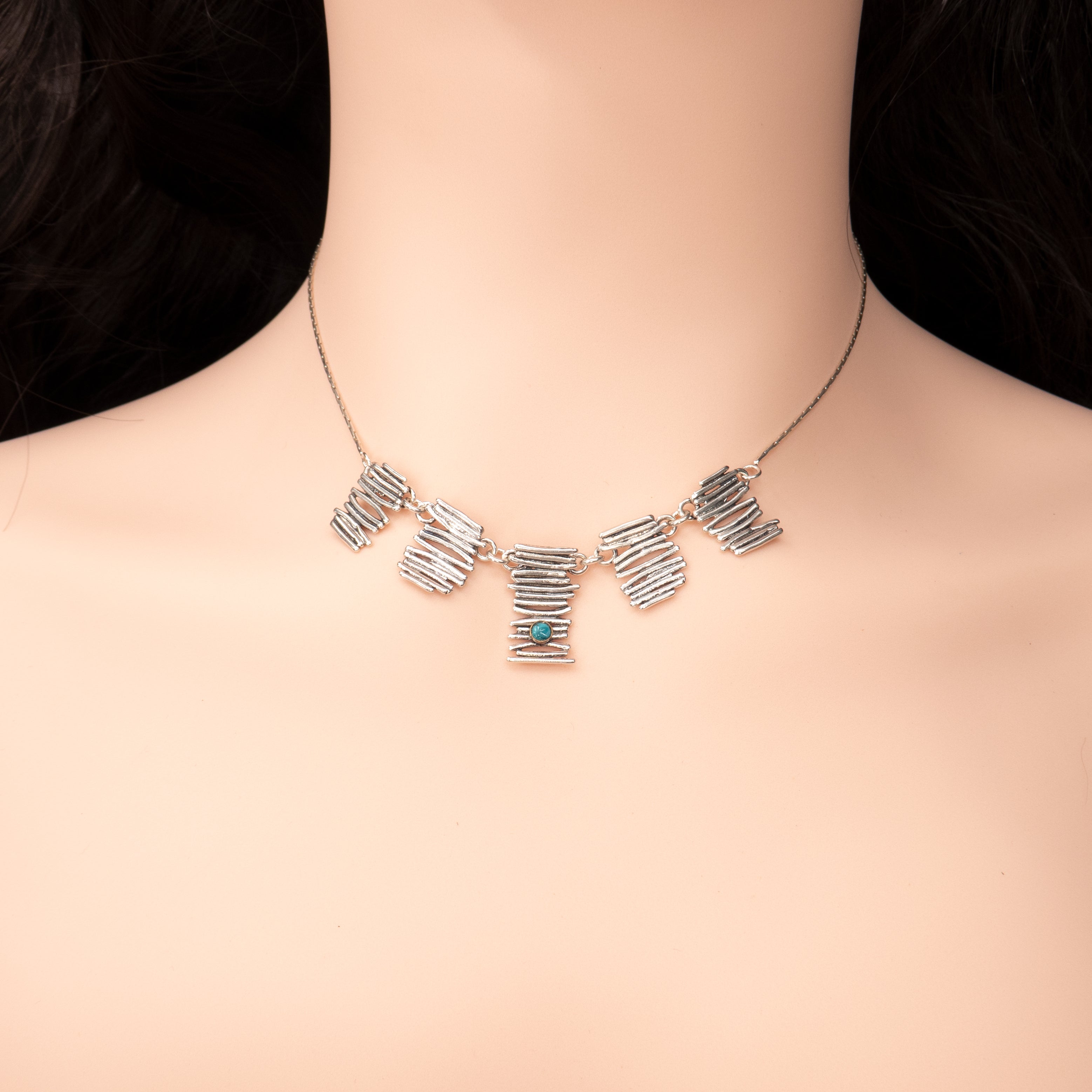 תמונה של שרשרת גיאומטרית מיוחדת מכסף, עם שלושה תליונים בצורת מבנה מופשט וטקסטורלי. כל תליון משובץ באבן טורקיז בגווני תכלת־טורקיז עזים, עם ברק עדין וטבעי. גוון האבן מקנה לתכשיט תחושת רעננות, חופש ואסתטיקה ים־תיכונית. מצולמת על צוואר ניטרלי שמבליט את הצבעים והצורות.


