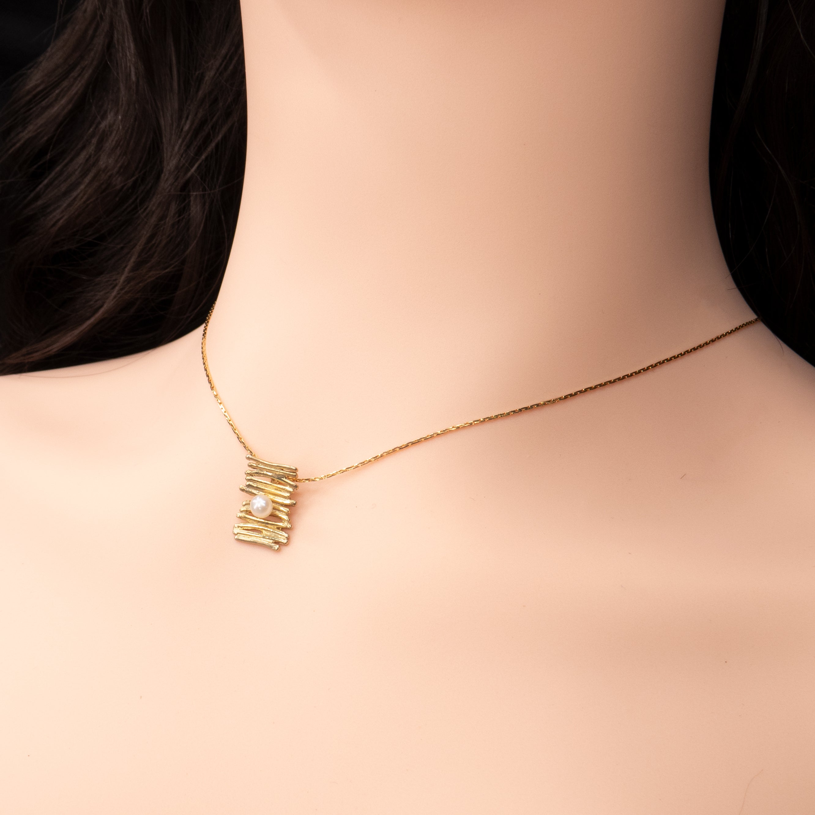שרשרת זהב מינימליסטית עם תליון בעיצוב אמנותי – שכבות זהב בגימור מחוספס ומתכתי, שביניהן משובצת פנינה קטנה מבריקה. עיצוב עדין ואלגנטי שמתאים לאישה שאוהבת שילוב בין טבע לפשטות מעודנת. קלאסי, רך ומודרני.