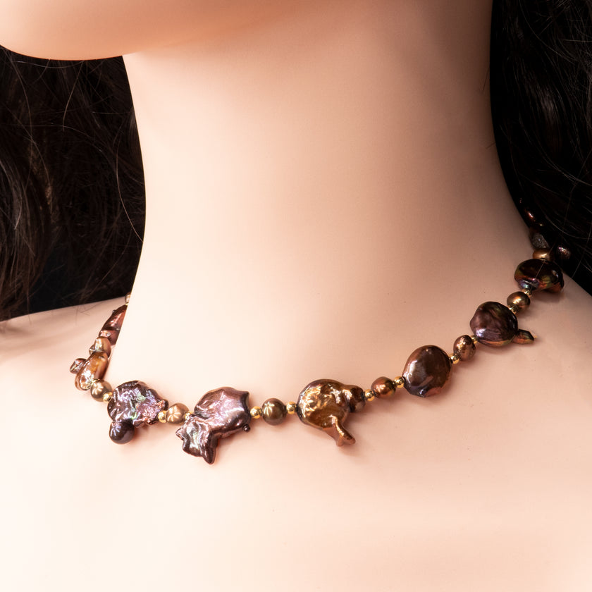 פריט בעיצוב לא שגרתי, מלא נוכחות המורכבת מפניני בארוק טבעיות בגוון שוקולד עמוק, עם אביזרים בציפוי זהב שמדגישים את צורתן הבלתי אחידה והמרקם החי של כל פנינה. הברק המטאלי החם של הפנינים משתלב באופן הרמוני עם הנגיעות המוזהבות, ויוצר תחושה של חומר חי ונושם. שילוב בין חוזק טבעי ליוקרה נינוחה – אידיאלי לאירוע ערב, להופעה עם אמירה או כמתנה מרשימה לאישה מיוחדת. פניני הבארוק, כל אחת עם אישיות משלה, הופכות את השרשרת הזו לשרשרת שלא דומה לשום דבר אחר – טבעית, אותנטית ומרשימה.