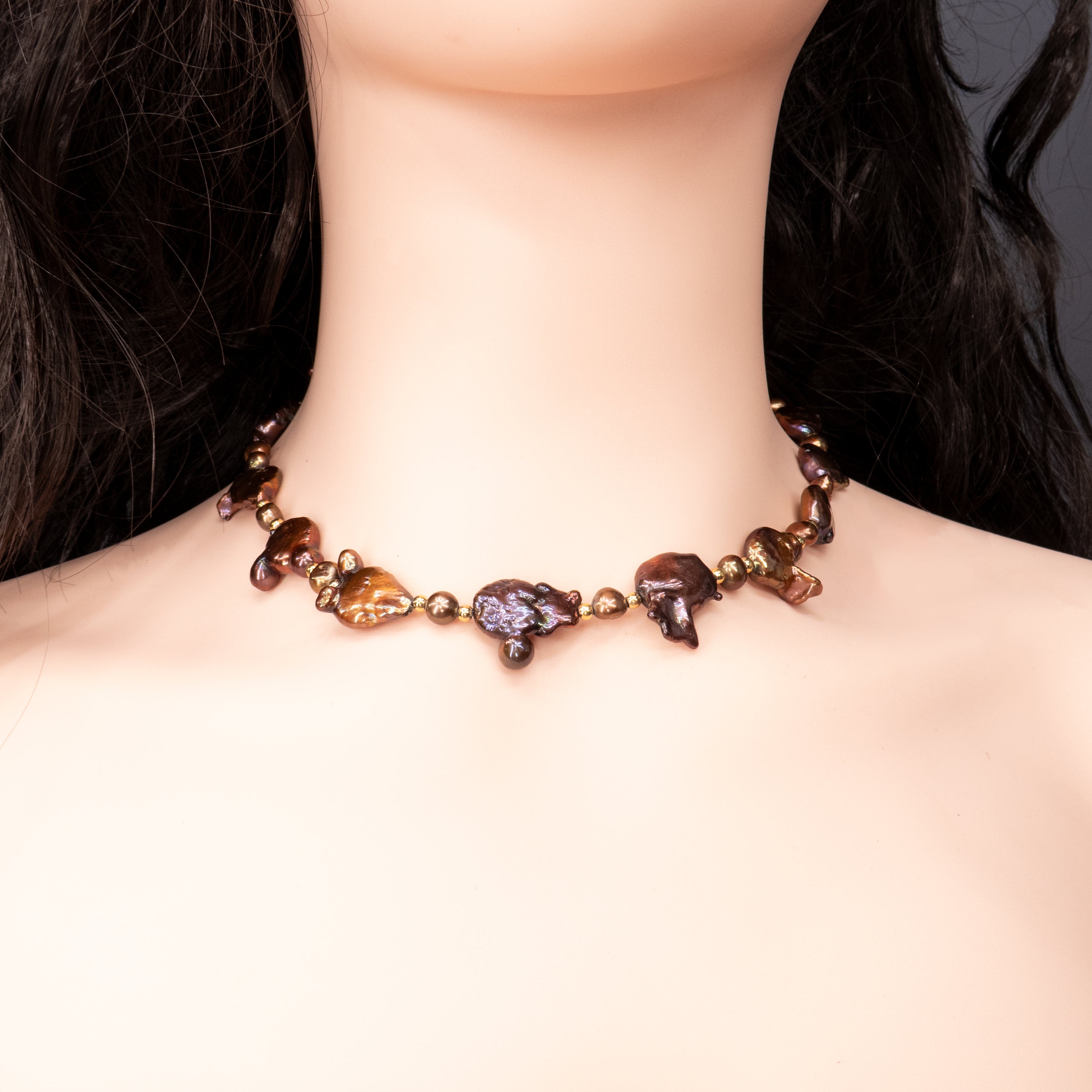 שרשרת נדירה שמדברת בעד עצמה המורכבת מפניני בארוק טבעיות בגוון שוקולד עמוק, עם אביזרים בציפוי זהב שמדגישים את צורתן הבלתי אחידה והמרקם החי של כל פנינה. הברק המטאלי החם של הפנינים משתלב באופן הרמוני עם הנגיעות המוזהבות, ויוצר מראה חם ועשיר שמזכיר אדמה וקליפה. שילוב בין חוזק טבעי ליוקרה נינוחה – אידיאלי לאירוע ערב, להופעה עם אמירה או כמתנה מרשימה לאישה מיוחדת. פניני הבארוק, כל אחת עם אישיות משלה, הופכות את השרשרת הזו לתכשיט שמבליט את הייחוד שלך בלי מילים.