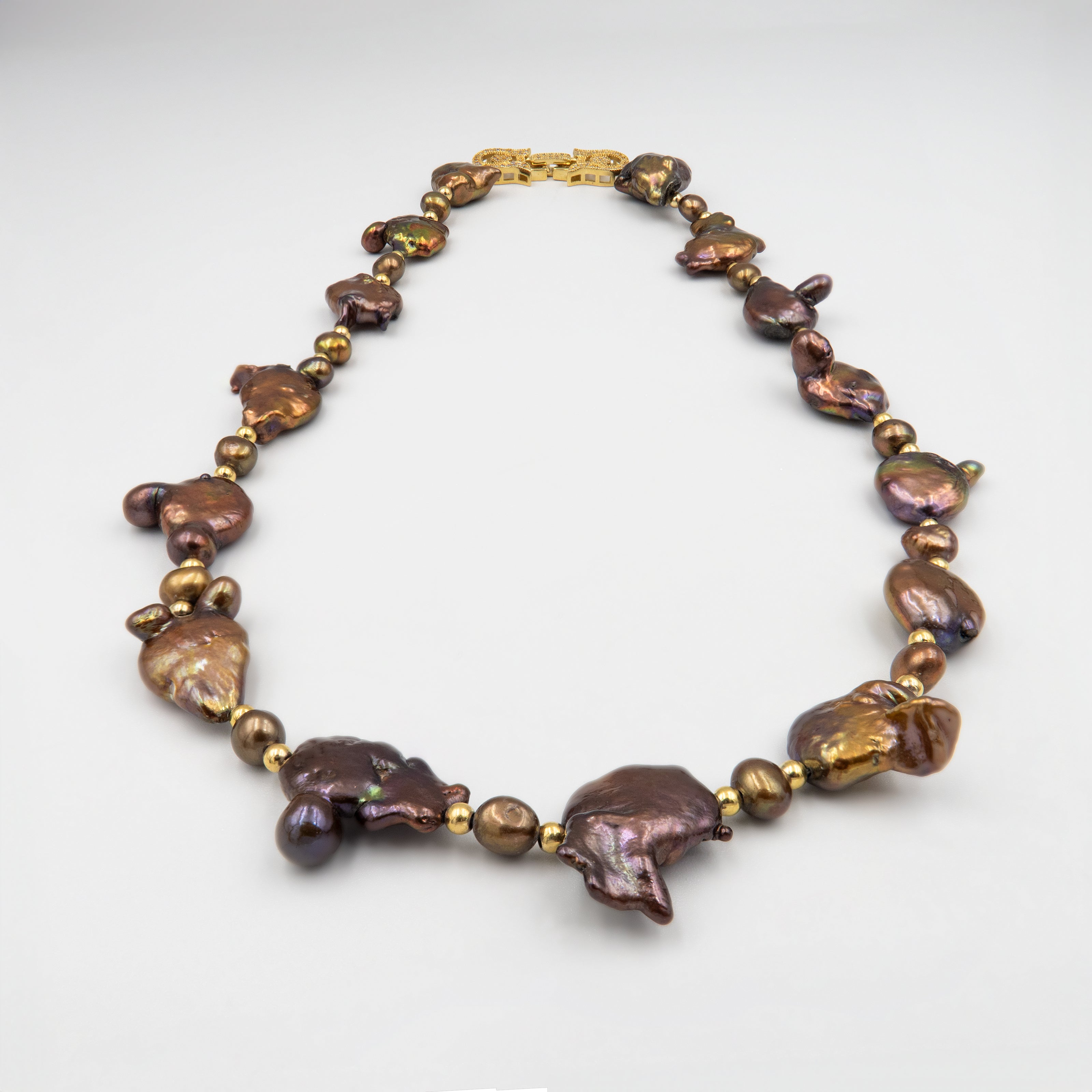 שרשרת נדירה שמדברת בעד עצמה המורכבת מפניני בארוק טבעיות בגוון שוקולד עמוק, עם אביזרים בציפוי זהב שמדגישים את צורתן הבלתי אחידה והמרקם החי של כל פנינה. הברק המטאלי החם של הפנינים משתלב באופן הרמוני עם הנגיעות המוזהבות, ויוצר ניחוח של טבע פראי ואלגנטי יחד. שילוב קלאסי ונועז כאחד – אידיאלי לאירוע ערב, להופעה עם אמירה או כמתנה מרשימה לאישה מיוחדת. פניני הבארוק, כל אחת עם אישיות משלה, הופכות את השרשרת הזו לשרשרת שלא דומה לשום דבר אחר – טבעית, אותנטית ומרשימה.