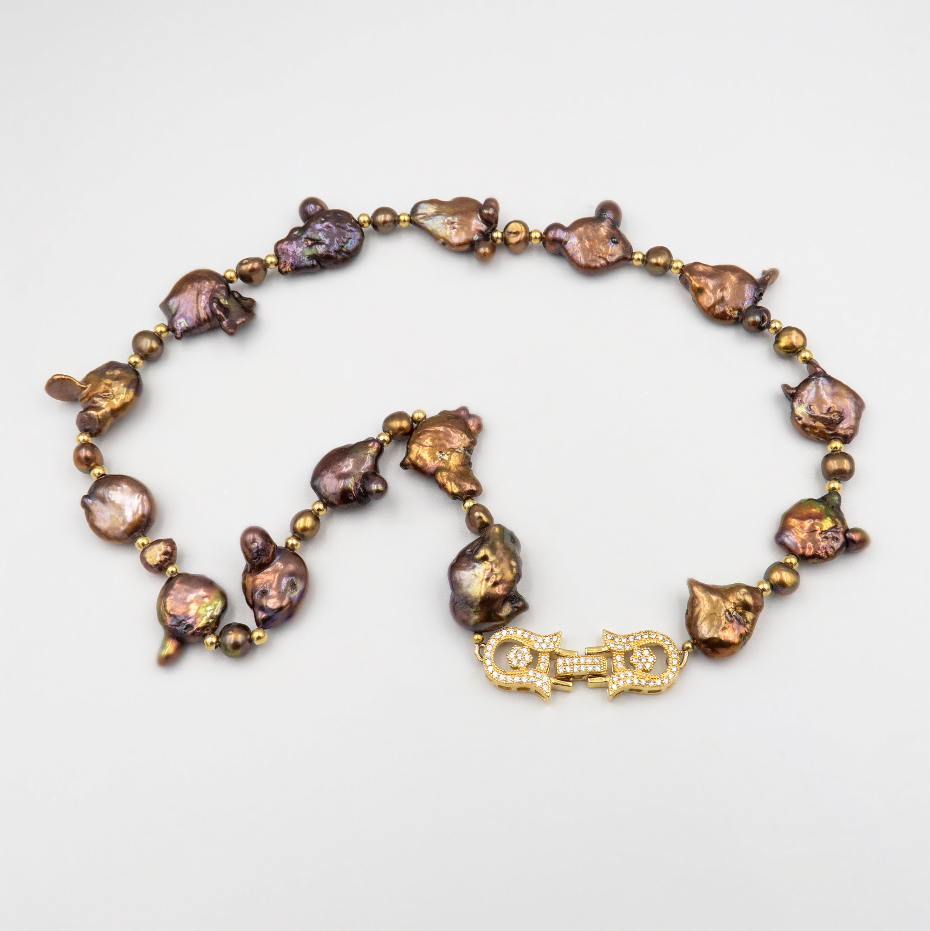 תכשיט בולט עם אופי טבעי המורכבת מפניני בארוק טבעיות בגוון שוקולד עמוק, עם אביזרים בציפוי זהב שמדגישים את צורתן הבלתי אחידה והמרקם החי של כל פנינה. הברק המטאלי החם של הפנינים משתלב באופן הרמוני עם הנגיעות המוזהבות, ויוצר ניחוח של טבע פראי ואלגנטי יחד. שילוב בין חוזק טבעי ליוקרה נינוחה – אידיאלי לאירוע ערב, להופעה עם אמירה או כמתנה מרשימה לאישה מיוחדת. פניני הבארוק, כל אחת עם אישיות משלה, הופכות את השרשרת הזו לתכשיט שמבליט את הייחוד שלך בלי מילים.