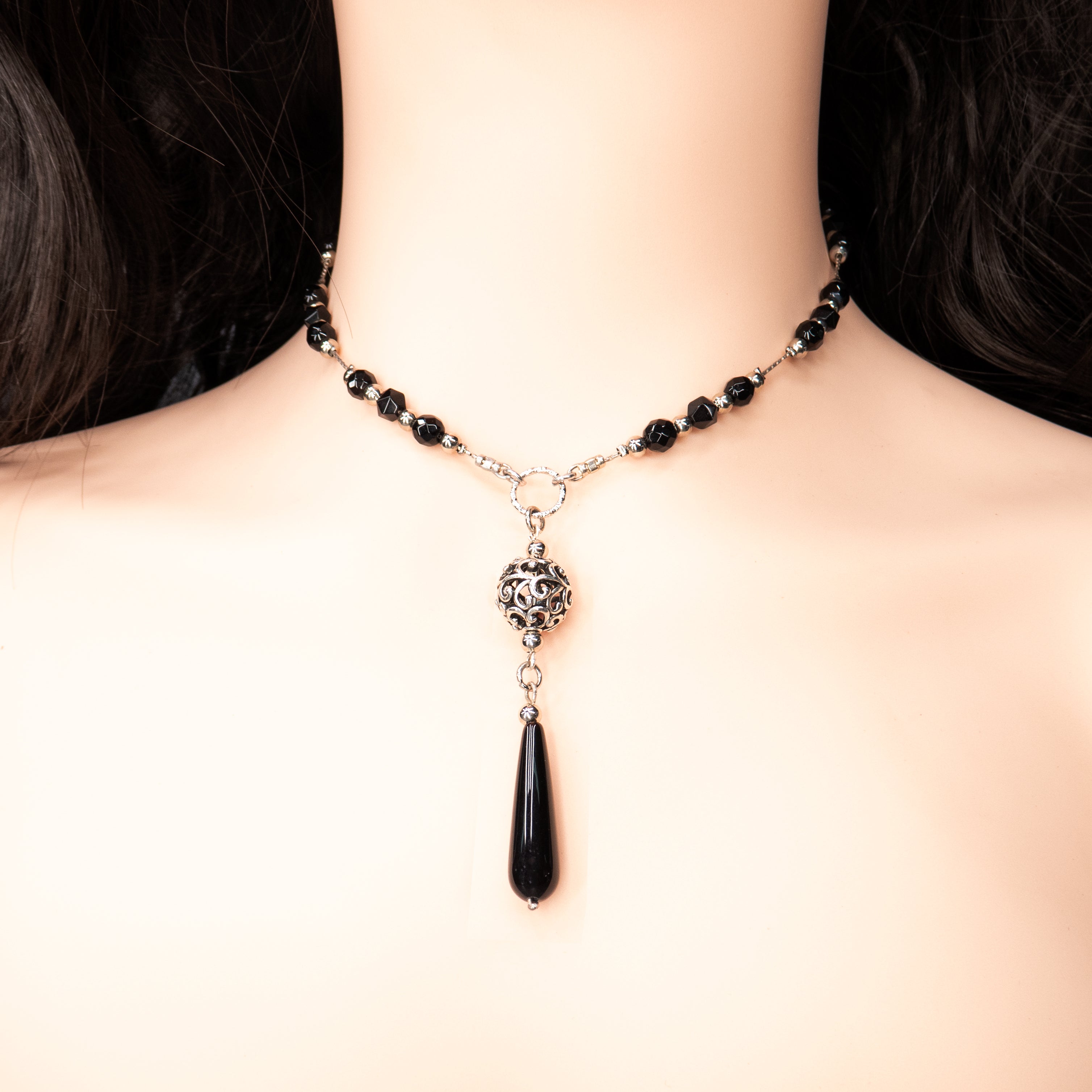 צילום תקריב של תכשיט כסף אלגנטי ונשי – שרשרת עם חרוזים בגוון אדום אוניקס סינתטי, בשילוב טבעות כסופות מעוצבות. תליון ארוך בצורת טיפה משתלשל מהמרכז, יוצר זרימה ואלגנטיות. מוצג על צוואר נקי ולבוש יומיומי בג’ינס.