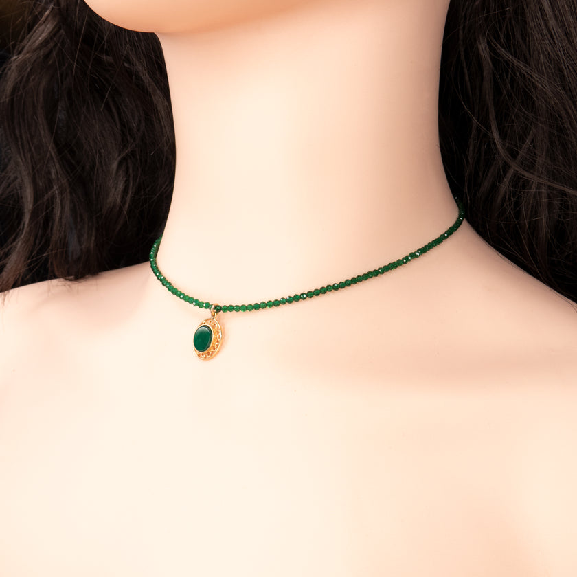קולר יוקרתי בגוון ירוק עמוק, עשוי חרוזים קטנים מבריקים עם תליון עגול מוזהב שבתוכו אבן ירוקה חלקה. עיצוב מדויק ונעים לעין, שמחמיא לכל גוון עור. צילום על רקע חולצה לבנה משדר ניקיון וסגנון. מושלם למתנה, לאירועים או להשלמת מראה מתוחכם.
