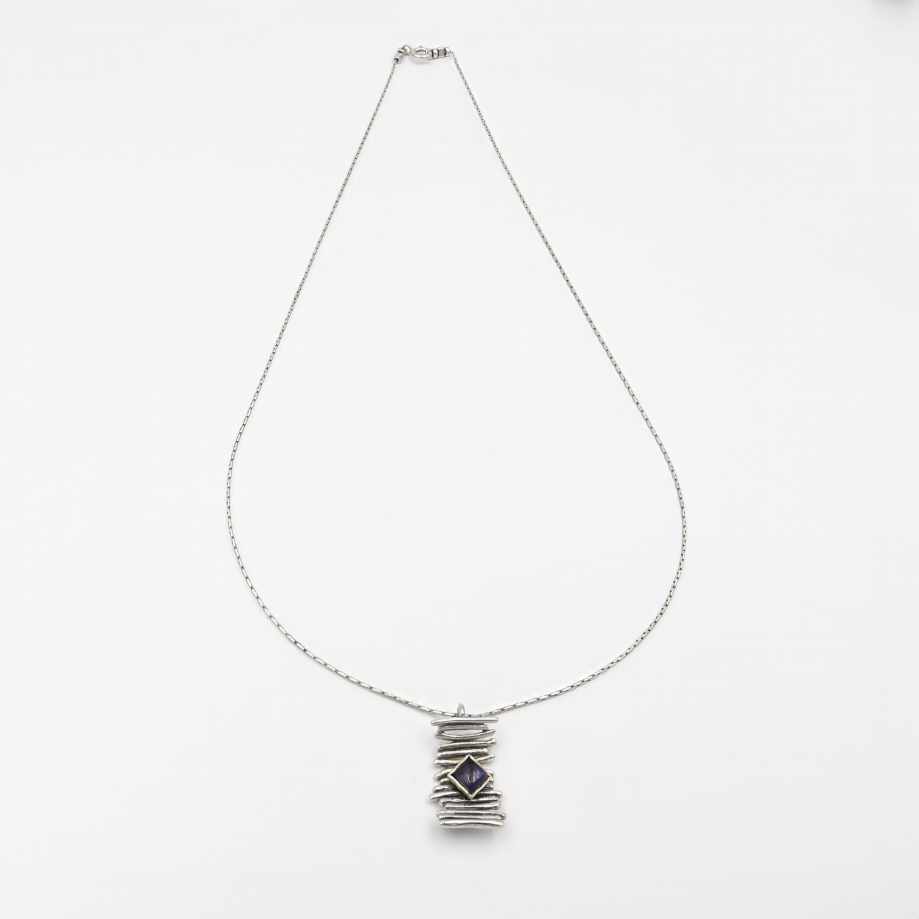 שרשרת מכסף סטרלינג בעיצוב מינימליסטי, עם קו מרכזי של חרוזים כסופים ותליון עגול קטן שתלוי מהם. בתוך התליון – אבן איולייט טבעית, בגוון כחול עמוק עם הבהקים סגולים עדינים, המלוטשת בגימור מבריק. האבן ידועה כאבן של אינטואיציה, איזון פנימי וראייה בהירה. תכשיט מושלם לשימוש יומיומי עם ערך אסתטי וסימבולי.

