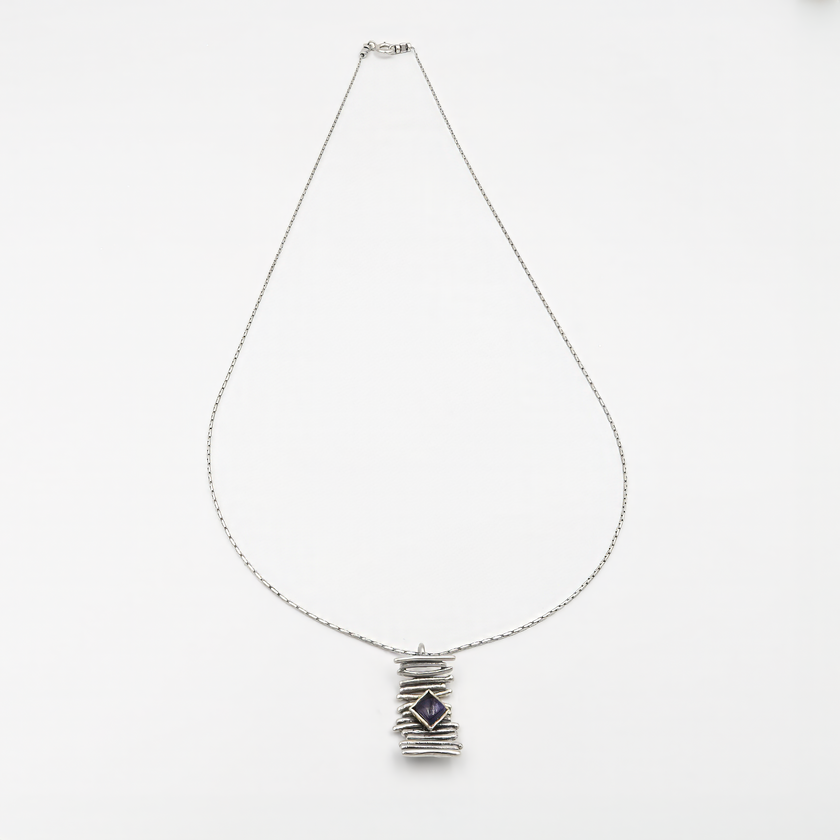 שרשרת מכסף סטרלינג בעיצוב מינימליסטי, עם קו מרכזי של חרוזים כסופים ותליון עגול קטן שתלוי מהם. בתוך התליון – אבן איולייט טבעית, בגוון כחול עמוק עם הבהקים סגולים עדינים, המלוטשת בגימור מבריק. האבן ידועה כאבן של אינטואיציה, איזון פנימי וראייה בהירה. תכשיט מושלם לשימוש יומיומי עם ערך אסתטי וסימבולי.

