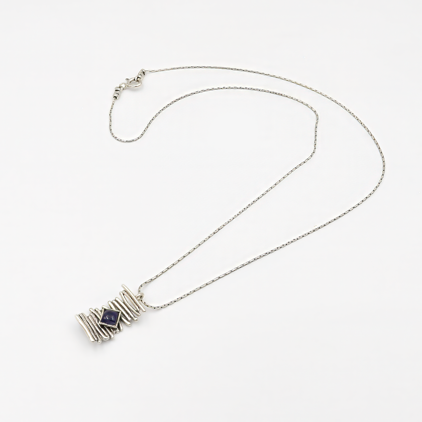 צילום תכשיט כסף קלאסי עם נוכחות שקטה: שרשרת דקה ועדינה עם חמישה חרוזים עגולים במרכזה, ומתחתיהם תליון עגול משובץ באבן איולייט כחולה-סגלגלה. האבן, בעלת ליטוש שטוח ושקיפות עדינה, משנה גוונים בהתאם לאור – מסגול כהה לכחול מעושן. התכשיט מושלם לנשים שאוהבות פריטים אלגנטיים עם טאץ' של קסם טבעי.

