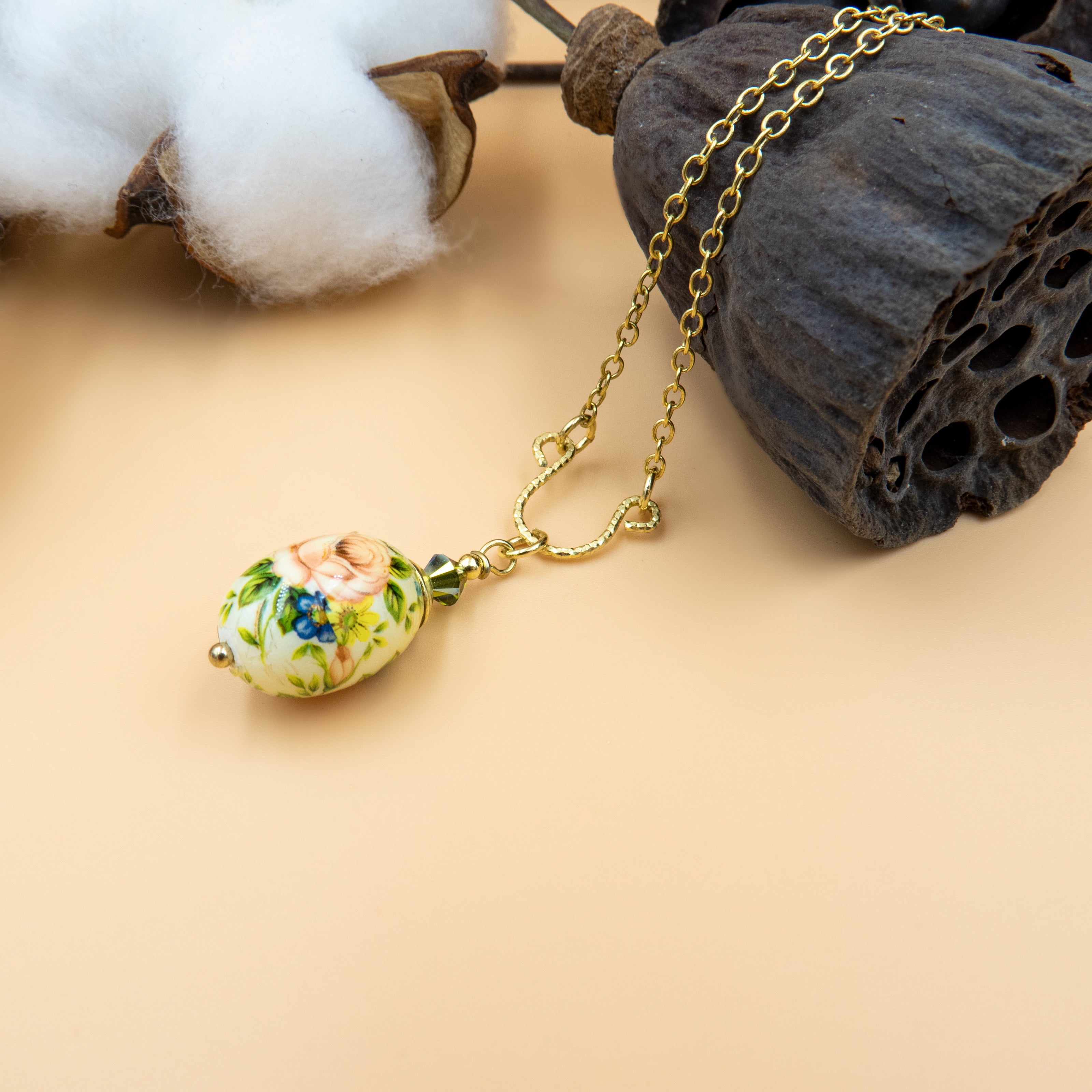 שרשרת בעיצוב רומנטי וקלסי, עם תליון פורצלן מעוצב בצורת ביצה קטנה וצבעונית. על גבי התליון – ציור פרחוני מרהיב בעבודת יד: שושנה ורודה מלאה מוקפת בעלים ירוקים ופרחים כחולים, בהשראת גני פרובאנס. החיבור לשרשרת מעוטר בחרוזים בגוון ירוק עמוק. תכשיט המשלב עדינות, נשיות וניחוח נוסטלגי.


