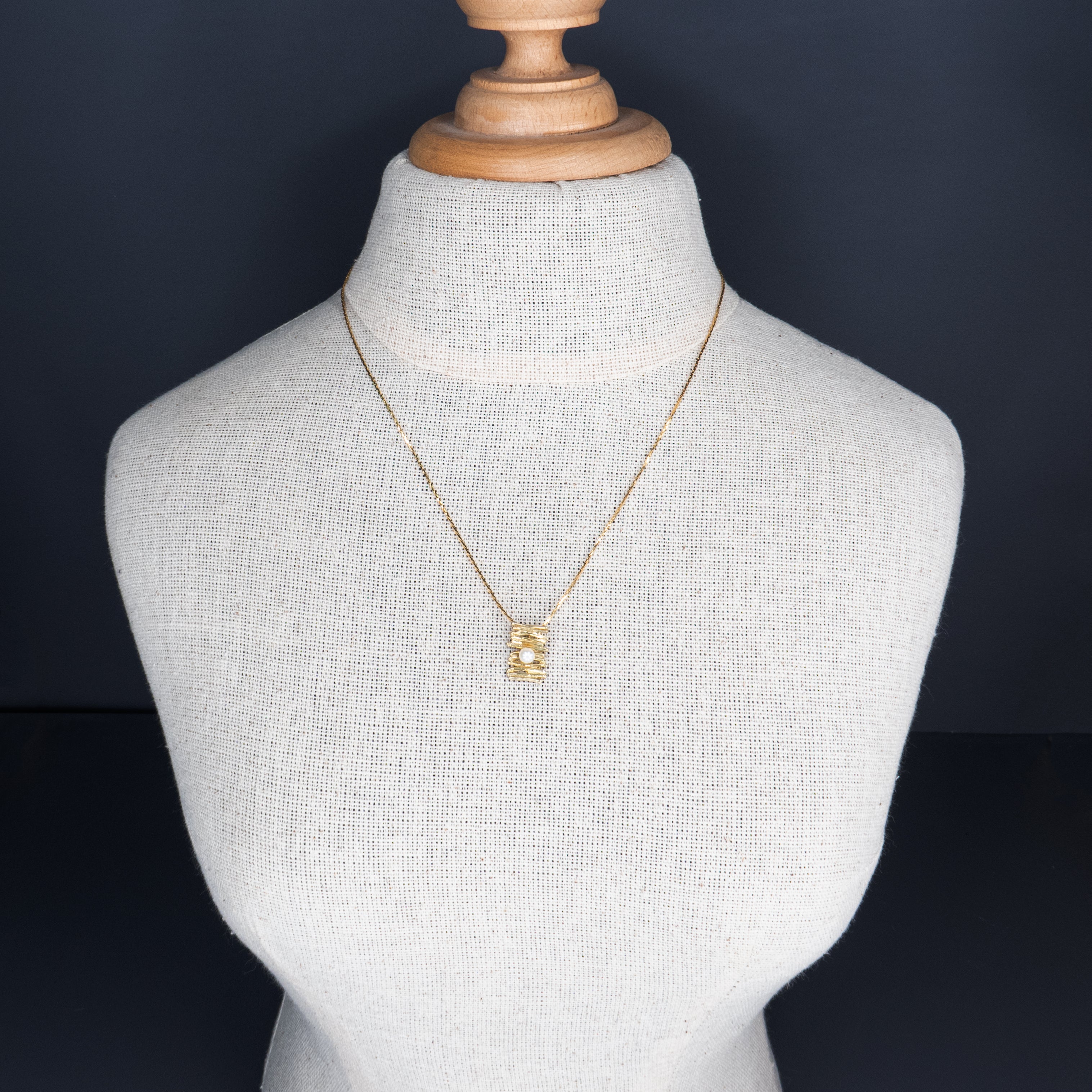 תליון ייחודי תלוי על שרשרת זהב דקה, בעיצוב א-סימטרי המזכיר שכבות של זהב טקסטורלי, כשבמרכזו פנינה לבנה קטנה ועדינה. מראה עכשווי עם נגיעות רכות וקלאסיות, המשלב בין מודרניזם לאלמנטים טבעיים. עיצוב מושלם למי שאוהבת פריטים עדינים אך מלאי אופי.