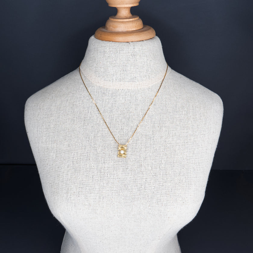 תליון ייחודי תלוי על שרשרת זהב דקה, בעיצוב א-סימטרי המזכיר שכבות של זהב טקסטורלי, כשבמרכזו פנינה לבנה קטנה ועדינה. מראה עכשווי עם נגיעות רכות וקלאסיות, המשלב בין מודרניזם לאלמנטים טבעיים. עיצוב מושלם למי שאוהבת פריטים עדינים אך מלאי אופי.