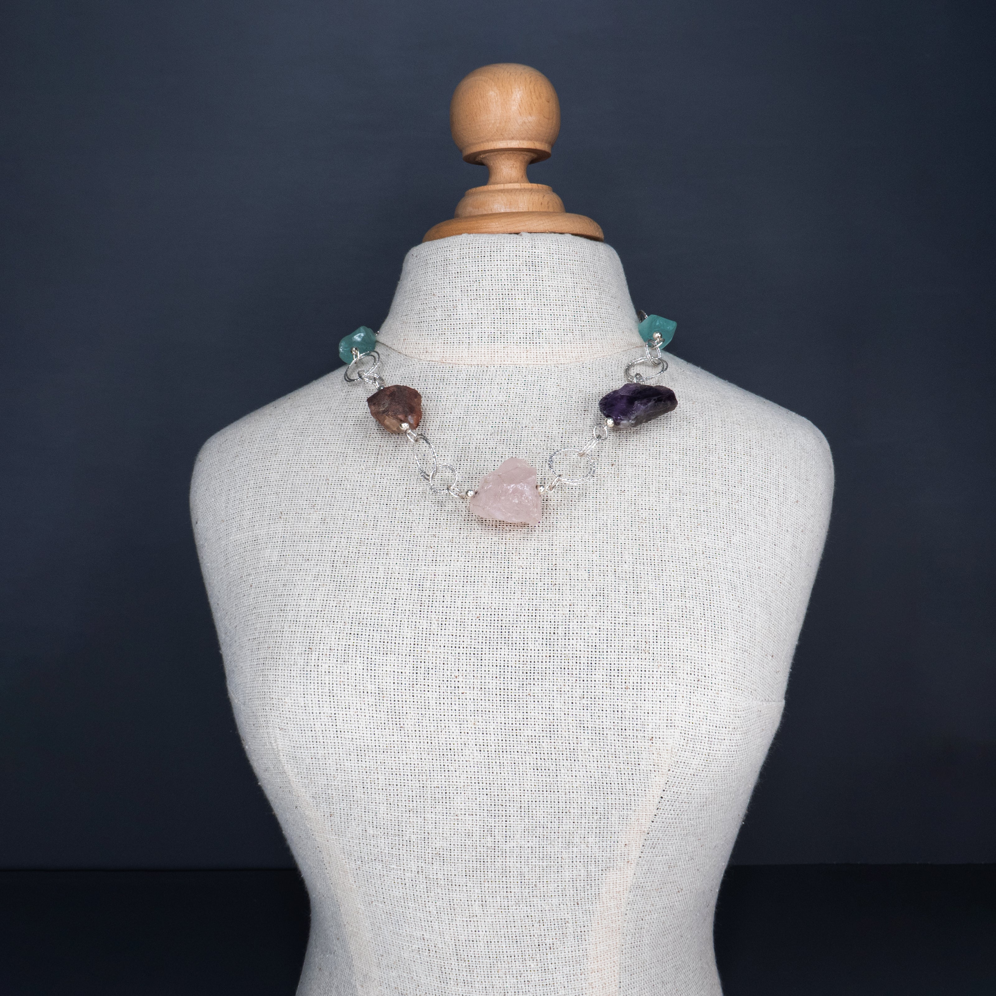 שרשרת כסף בעבודת יד שמשלבת מגוון עשיר של קריסטלים טבעיים – אמטיסט בגוון סגול עמוק, רוז קוורץ ורדרד ורך, פלואוריט בגוני ירוק וסגול שקופים, וקרנליאן חם בצבע כתום־אדמדם. ההשילוב הטבעי מקרין חום ונשיות עם עומק רגשי ואנרגטי, וכל אבן מוסיפה שכבה משלה של משמעות ונוכחות. השרשרת עוצבה כך שכל אבן תוכל לנשום, ומשלב ביניהן תוך כדי משחק של צבעים, טקסטורות ושקיפויות. השרשרת לנשים שמחפשות עומק ומשמעות באביזרים שלהן, כאלה שמתחברות לעוצמה שקטה ולסטייל ייחודי – וגם לאלו שמחפשות איזון, השראה ורוך. תכשיט שהוא גם יופי וגם חוויה