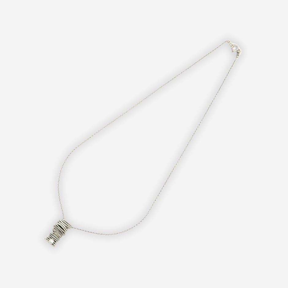 שרשרת מכסף בעיצוב ייחודי ואלגנטי עם תליון בעבודת יד בצורת גליל, בנוי משכבות של חוטי כסף המלופפים זה על זה באקראיות מחושבת. בקצה התחתון של התליון שובצה פנינה קטנה ועדינה, שמוסיפה נגיעה רכה לעיצוב הגולמי. התכשיט כולו מעוצב בסגנון מודרני ומתאים לנשים שאוהבות אמירה אישית עדינה אך מתוחכמת.