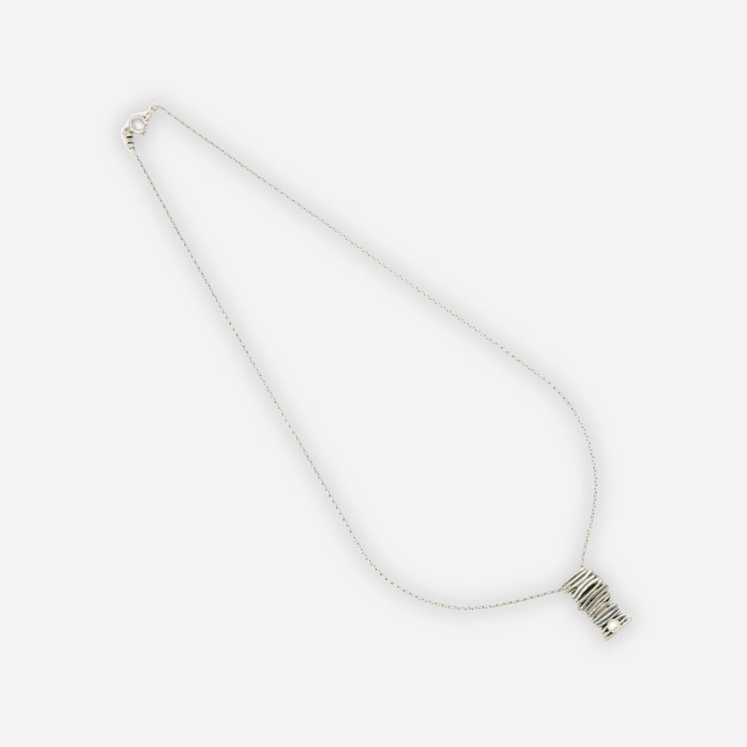 תליון כסף מרשים בעיצוב פיסולי: שכבות של חוטי כסף מלופפים ליצירת גליל טקסטורלי מרהיב, תלוי משרשרת עדינה ודקה. בבסיסו שיבוץ פנינה קטנה בצבע לבן שמנת. עיצוב שמשדר איכות, ניקיון ועידון. מושלם כשילוב לתלבושות יומיומיות עם טאץ' אלגנטי או כתכשיט למראה ערב נקי.