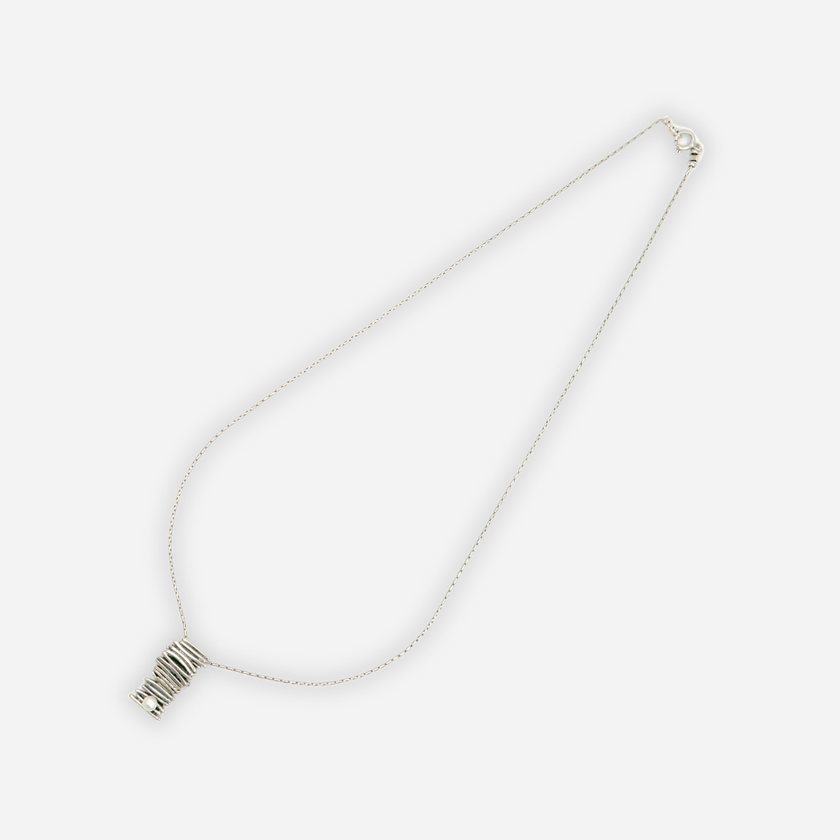 שרשרת מכסף בעיצוב ייחודי ואלגנטי עם תליון בעבודת יד בצורת גליל, בנוי משכבות של חוטי כסף המלופפים זה על זה באקראיות מחושבת. בקצה התחתון של התליון שובצה פנינה קטנה ועדינה, שמוסיפה נגיעה רכה לעיצוב הגולמי. התכשיט כולו מעוצב בסגנון מודרני ומתאים לנשים שאוהבות אמירה אישית עדינה אך מתוחכמת.