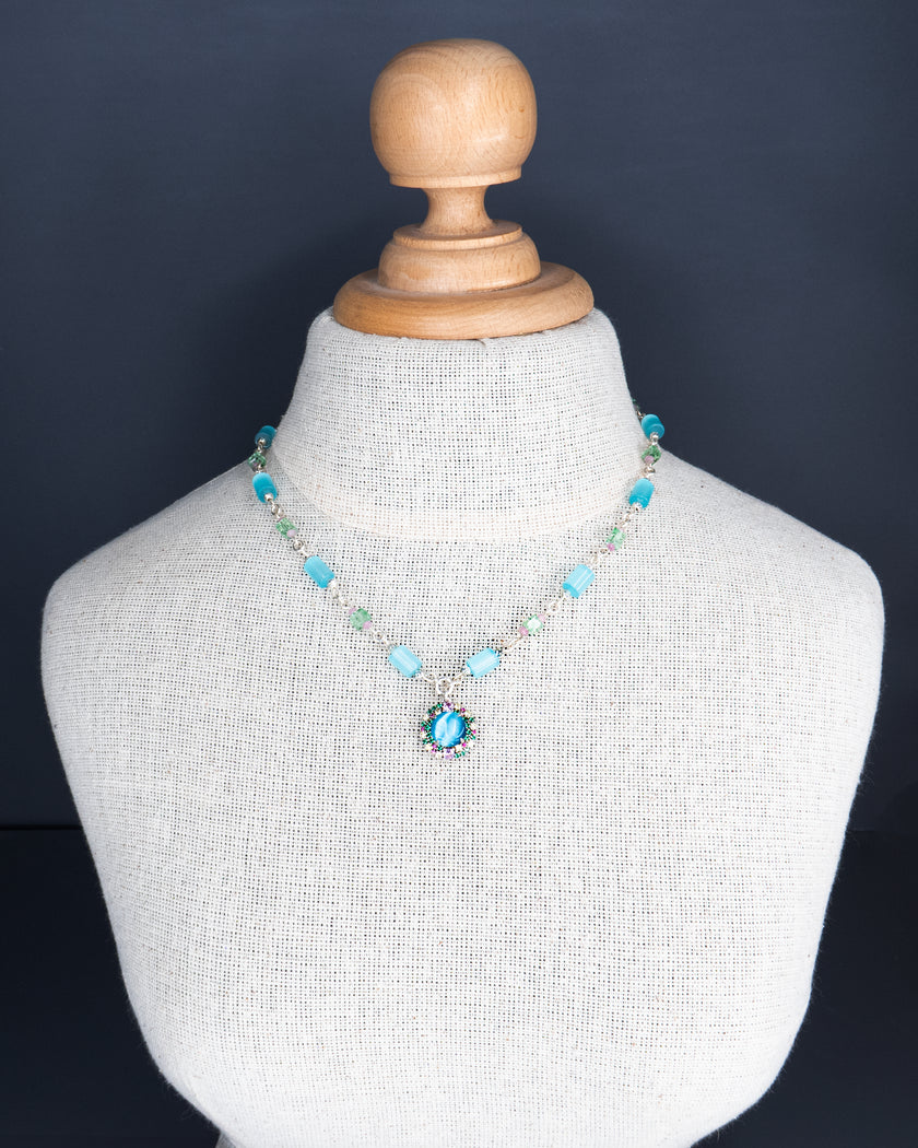 שרשרת בהירה ומרעננת, עם עיצוב טבעי ונשי – תליון פרח בגימור אלגנטי על רקע גווני תכלת שמיימיים. שילוב צבעים שמחמיא לגווני עור שונים ומאיר את הפנים באור רך ונעים.