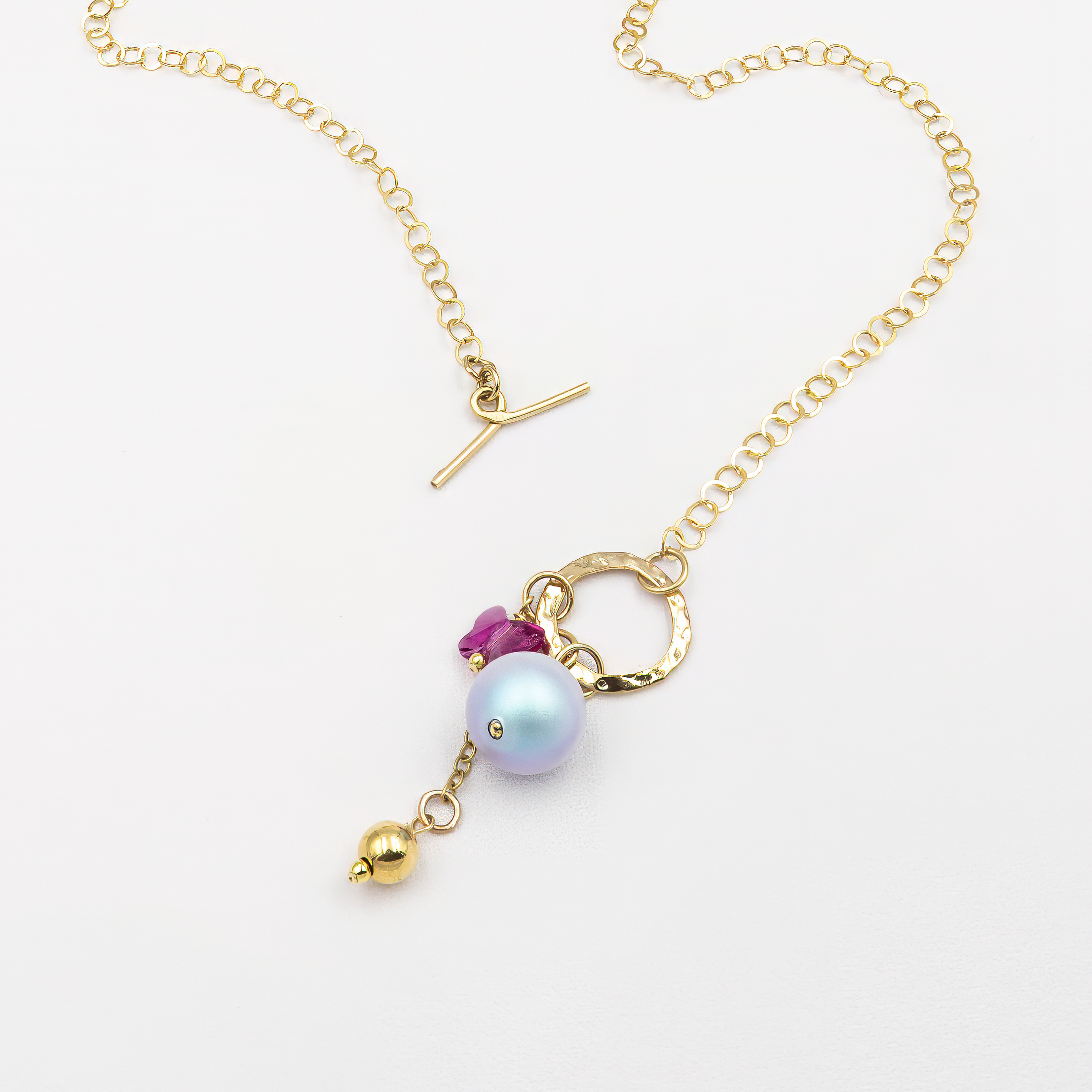 תליון ייחודי המורכב מפנינה בגוון כחול-סגלגל, חרוז פרפר ורוד ותליון מתכתי מוזהב, תלויים על סוגר טוגל מוזהב שממוקם בקדמת שרשרת חוליות זהובה. עיצוב אלגנטי עם נגיעה של פנטזיה וצבע.