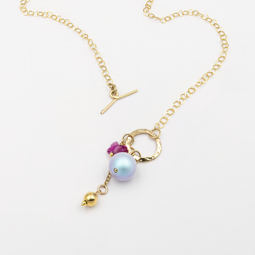 תליון ייחודי המורכב מפנינה בגוון כחול-סגלגל, חרוז פרפר ורוד ותליון מתכתי מוזהב, תלויים על סוגר טוגל מוזהב שממוקם בקדמת שרשרת חוליות זהובה. עיצוב אלגנטי עם נגיעה של פנטזיה וצבע.