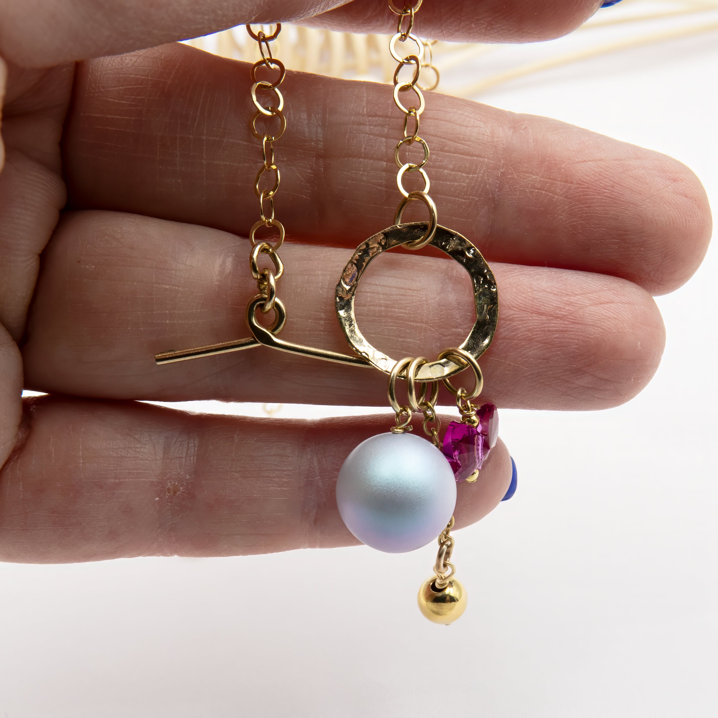 שרשרת בעיצוב קליל ומלא אופי: פנינה סגלגלה, פרפר ורוד חינני ותליון זהוב תלויים יחד על סוגר טוגל מוזהב בחלק הקדמי של שרשרת חוליות. עיצוב שמחבר צבעים רכים עם ברק מטאלי בצורה הרמונית.