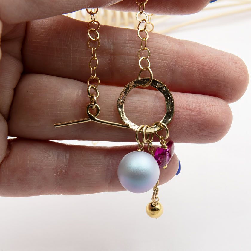 שרשרת בעיצוב קליל ומלא אופי: פנינה סגלגלה, פרפר ורוד חינני ותליון זהוב תלויים יחד על סוגר טוגל מוזהב בחלק הקדמי של שרשרת חוליות. עיצוב שמחבר צבעים רכים עם ברק מטאלי בצורה הרמונית.