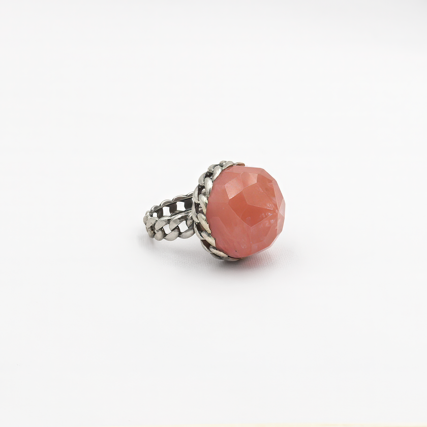 טבעת כסף עוצמתית מלאת תשומת לב, מקושטת באבן גדולה בגוון ורוד־קורל עם חיתוך פאות (faceted) שמבליט את הזוהר את הברק והעומק של האבן. העיצוב משלב בסיס כסף בעבודת חריטה בדוגמה קלועה, המעניק לטבעת מראה חזק אך אלגנטי, שמזכיר טבעת שרשרת או סגנון בוהו וינטג' מתוחכם. האבן הגדולה הופכת את הטבעת לפריט נועז, כזה שלא עובר מתחת לרדאר, אך שומר על איזון אסתטי. גוון האבן מחמיא לעור, מתאים לקיץ ולחורף כאחד, ויוצר ניגוד יפהפה עם גוון המתכת. תכשיט מיוחד שמדגיש אישיות, חוש אסתטי ואמירה אישית לא שגרתית. מושלמת כטבעת מתנה, ליום־יו