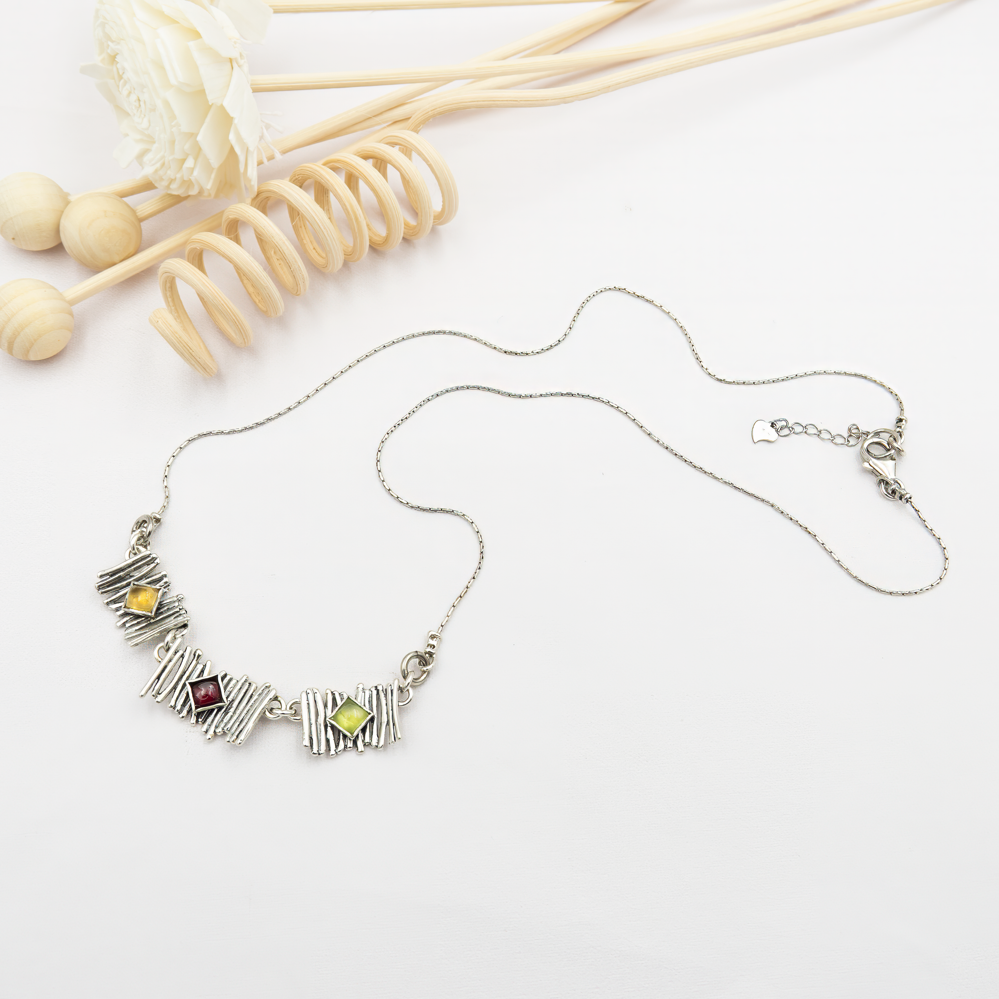 שרשרת כסף ייחודית עם שלושה אלמנטים טקסטורליים בסגנון מודרני. במרכז שיבוץ של אבן פרידוט ירוקה בחיתוך מרובע, ובצדדים שיבוצים עגולים של אותה אבן. הפרידוט, בגוון ירוק רענן, מוסיף מגע של טבע, איזון ואנרגיה חיובית. העיצוב הגאומטרי פוגש את צבעוניות האבן, ויוצר תכשיט עם נוכחות רגועה ומודרנית.
