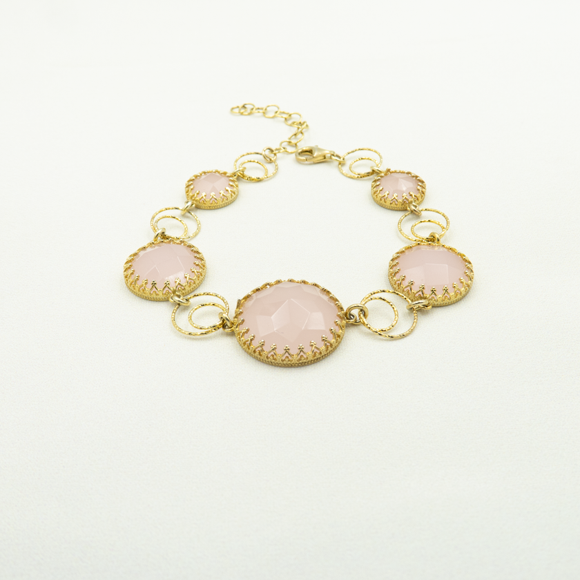 צמיד יוקרתי בגוון זהב חם, משובץ באופליט ורוד עדין – אבן סינתטית בגוון פסטלי רך עם ברק חלבי. האבנים משובצות בצורת מעגל במסגרת דקורטיבית, כאשר הגדולה במרכז מהווה מוקד תשומת הלב. העיצוב מחבר בין קלאסיקה לנשיות מודרנית ומתאים כמתנה ליום הולדת, ליום נישואין או לאירוע מיוחד. תכשיט מרשים שמוסיף אור ורוך לכל הופעה, ומחמיא במיוחד לגווני עור בהירים.

