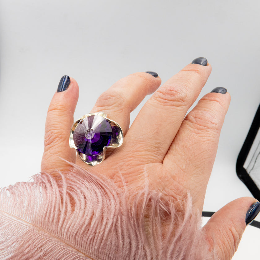 טבעת כסף בעבודת יד, מעוטרת בקריסטל סגול בגוון המזכיר את אבן האמטיסט – אור סגול רגשי שנע בין לבנדר עדין לסגול כהה. האבן חתוכה בפאות מדויקות ויוצרת משחקי אור שמעניקים לה זוהר פנימי שקט. השילוב בין גוון האבן האצילי לבין מתכת הכסף המלוטשת מעניק לטבעת תחושת הרמוניה נשית, בין קלאסיקה לאנרגיה מודרנית. התכשיט מתאים לנשים שמחפשות עומק, אופי רגשי עמוק שאינה מובנת מאליה. קריסטל בגוון אמטיסט מסמל איזון נפשי – ומתאים כתוספת למראה יומיומי מלא חן או כתכשיט עם משמעות לערב מיוחד.