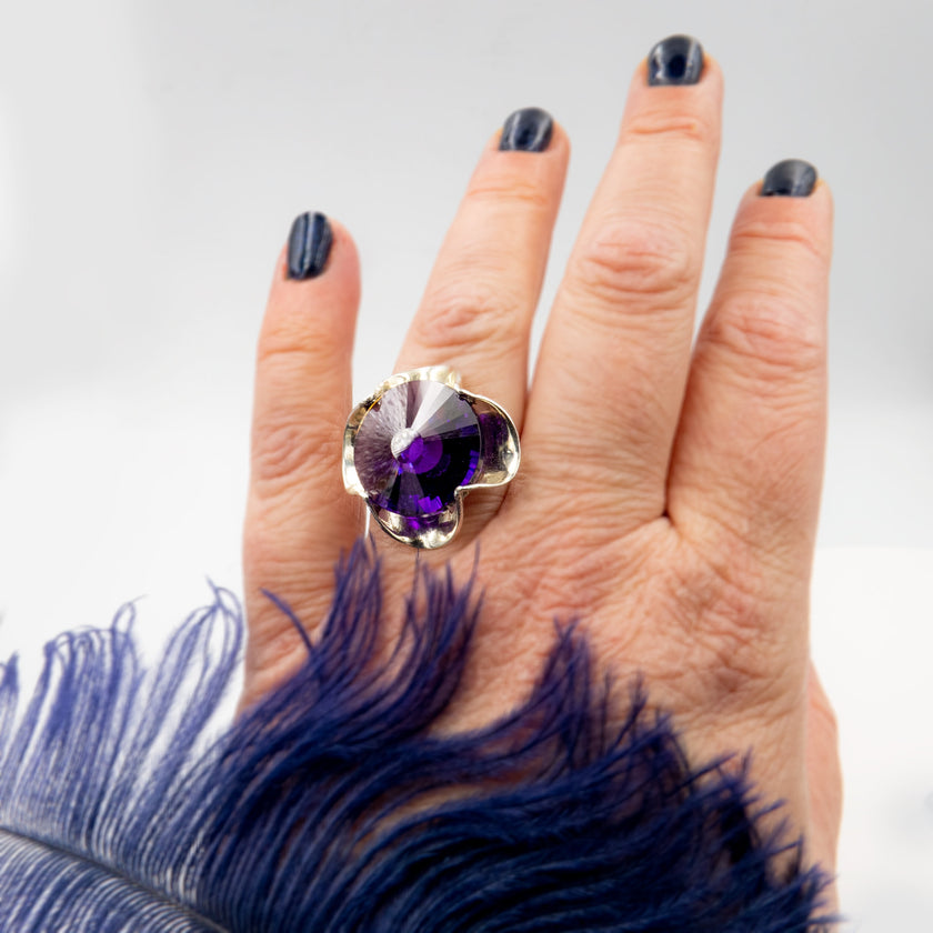 טבעת כסף בעבודת יד, כוללת בקריסטל סגול בגוון המזכיר את אבן האמטיסט – סגול מלכותי שנע בין לבנדר עדין לסגול כהה. האבן חתוכה בפאות מדויקות ויוצרת משחקי אור שמעניקים לה אור רך ומרגש. השילוב בין גוון האבן האצילי לבין מתכת הכסף המלוטשת מעניק לטבעת חיבור בין חוזק לעדינות, בין קלאסיקה לאנרגיה מודרנית. התכשיט מתאים לנשים שמחפשות עומק, הבעה אישית ומיוחדת שאינה מובנת מאליה. קריסטל בגוון אמטיסט מסמל חכמה אינטואיטיבית – ומתאים כתוספת למראה יומיומי מלא חן או כתכשיט עם משמעות לערב מיוחד.