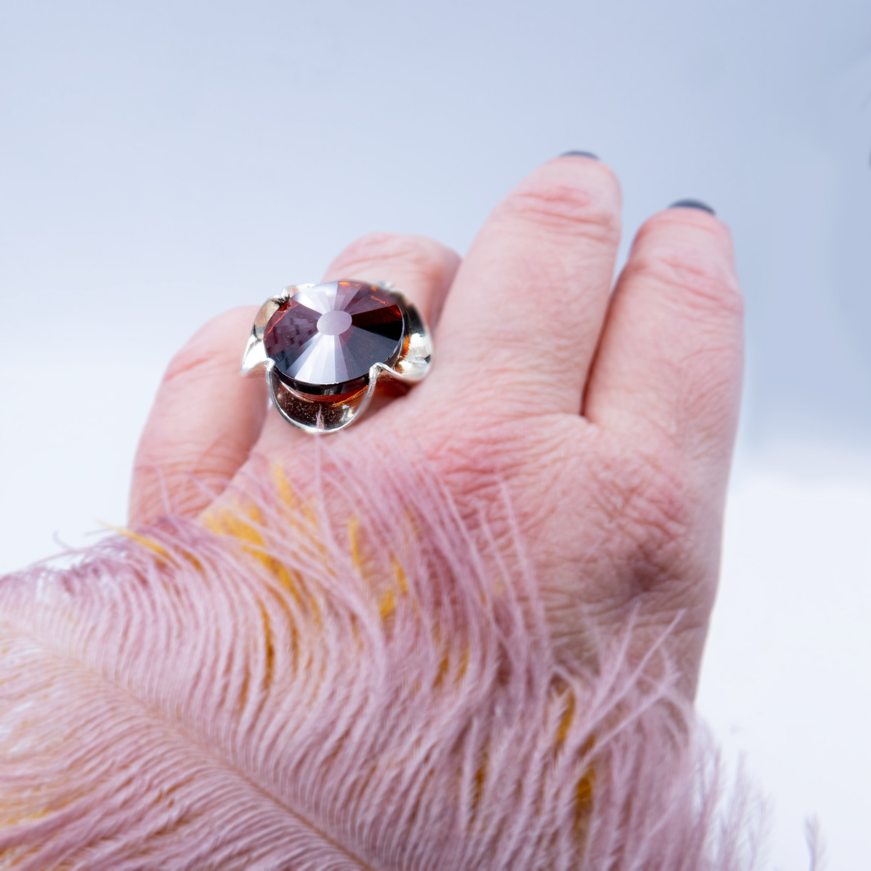 טבעת כסף מעוצבת בעבודת יד, משובצת בקריסטל בגוון יין עמוק המדמה את אבן הגארנט – צבע יין עשיר עם עומק רגשי וניצוץ עמוק. האבן מלוטשת בפאות רבות, מה שמעניק לה נצנוץ פנימי וזוהר משתנה בהתאם לזוויות האור. העיצוב של הטבעת שומר על איזון בין עיצוב על-זמני לבין אמירה עדינה, ומתאים לנשים שמבקשות תכשיט עם משמעות, עומק וסגנון אישי. צבע האבן משתלב נהדר עם גוון המתכת הכסופה, ויוצר מראה חם, נשי ועוצמתי. הטבעת מתאימה גם כפריט יום־יומי יוקרתי וגם כתוספת מרשימה למראה ערב – רעיון מתנה מרגש כמתנה רומנטית או כאמירה אישית.