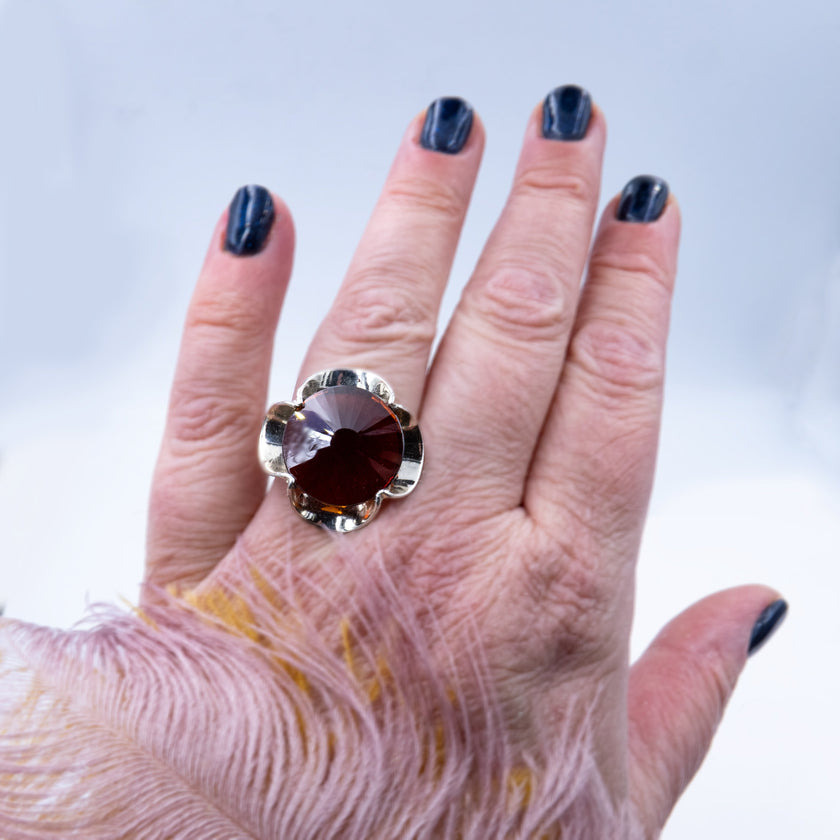 טבעת כסף מעוצבת בעבודת יד, משובצת בקריסטל בגוון בורדו המדמה את אבן הגארנט – צבע יין עשיר עם עומק רגשי וזוהר פנימי. האבן מלוטשת בפאות רבות, מה שמעניק לה נצנוץ פנימי וזוהר משתנה בהתאם לזוויות האור. העיצוב של הטבעת שומר על איזון בין עיצוב על-זמני לבין עוצמה שקטה, ומתאים לנשים שמבקשות תכשיט עם משמעות, עומק וסגנון אישי. צבע האבן משתלב נהדר עם גוון המתכת הכסופה, ויוצר מראה חם, נשי ועוצמתי. הטבעת מתאימה גם כפריט יום־יומי יוקרתי וגם כתוספת מרשימה למראה ערב – רעיון מתנה מרגש כמתנה רומנטית או כאמירה אישית.
