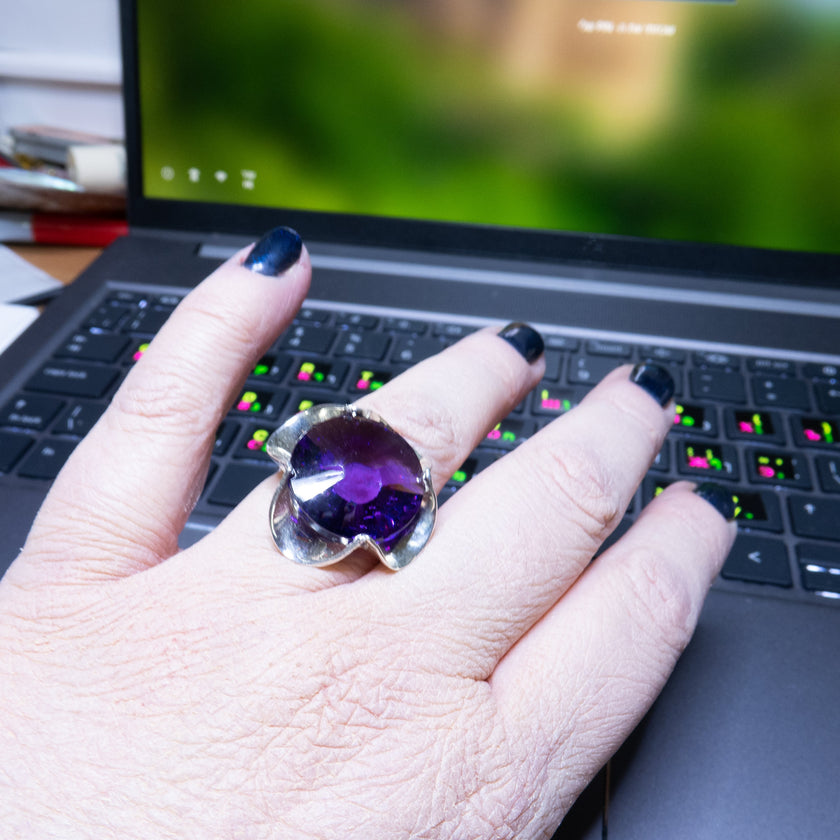 טבעת כסף בעבודת יד, מעוטרת בקריסטל סגול בגוון המזכיר את אבן האמטיסט – סגול מלכותי שנע בין לבנדר עדין לסגול כהה. האבן חתוכה בפאות מדויקות ויוצרת משחקי אור שמעניקים לה אור רך ומרגש. השילוב בין גוון האבן האצילי לבין מתכת הכסף המלוטשת מעניק לטבעת שילוב של רגש ואלגנטיות, בין קלאסיקה לאנרגיה מודרנית. התכשיט מתאים לנשים שמחפשות עומק, אופי רגשי עמוק שאינה מובנת מאליה. קריסטל בגוון אמטיסט מסמל חיבור רגשי עמוק – ומתאים כתוספת למראה יומיומי מלא חן או כתכשיט עם משמעות לערב מיוחד.