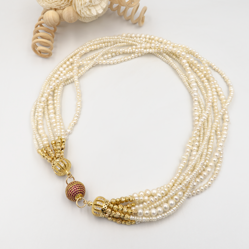 עיצוב אלגנטי עם פנינים טבעיות וסוגר בעיצוב ייחודי. כל שורת פנינים מוסיפה לתכשיט מימד של תנועה, עומק ויוקרה קלאסית – יחד הן יוצרות סטייל חגיגי עם מראה קלאסי. הברק הטבעי של הפנינים משתלב עם האלמנטים המוזהבים לרושם אלגנטי עם טוויסט עכשווי. הסוגר הייחודי, המעוטר באבני קריסטל קטנות בגוון יין עמוק, מהווה מוקד עיצובי שמוסיף עניין ותחושת פאר. שרשרת אידאלית לאירוע חגיגי, חתונה או ערב חשוב – שרשרת שמובילה את ההופעה בעדינות ובחן.