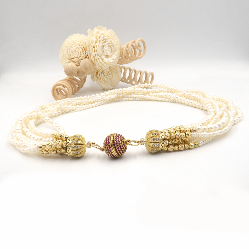 עיצוב אלגנטי עם פנינים טבעיות וסוגר בעיצוב ייחודי. כל שורת פנינים מוסיפה לתכשיט מימד של תנועה, עומק ויוקרה קלאסית – יחד הן יוצרות מראה דרמטי עם רוך נשי. הברק הטבעי של הפנינים משתלב עם האלמנטים המוזהבים לתחושת יוקרה על־זמנית. הסוגר הייחודי, המעוטר באבני קריסטל קטנות בגוון יין עמוק, מהווה מוקד עיצובי שמוסיף עניין ותחושת פאר. שרשרת אידאלית לאירוע חגיגי, חתונה או ערב חשוב – אביזר מרכזי בלוק חגיגי ונשי.