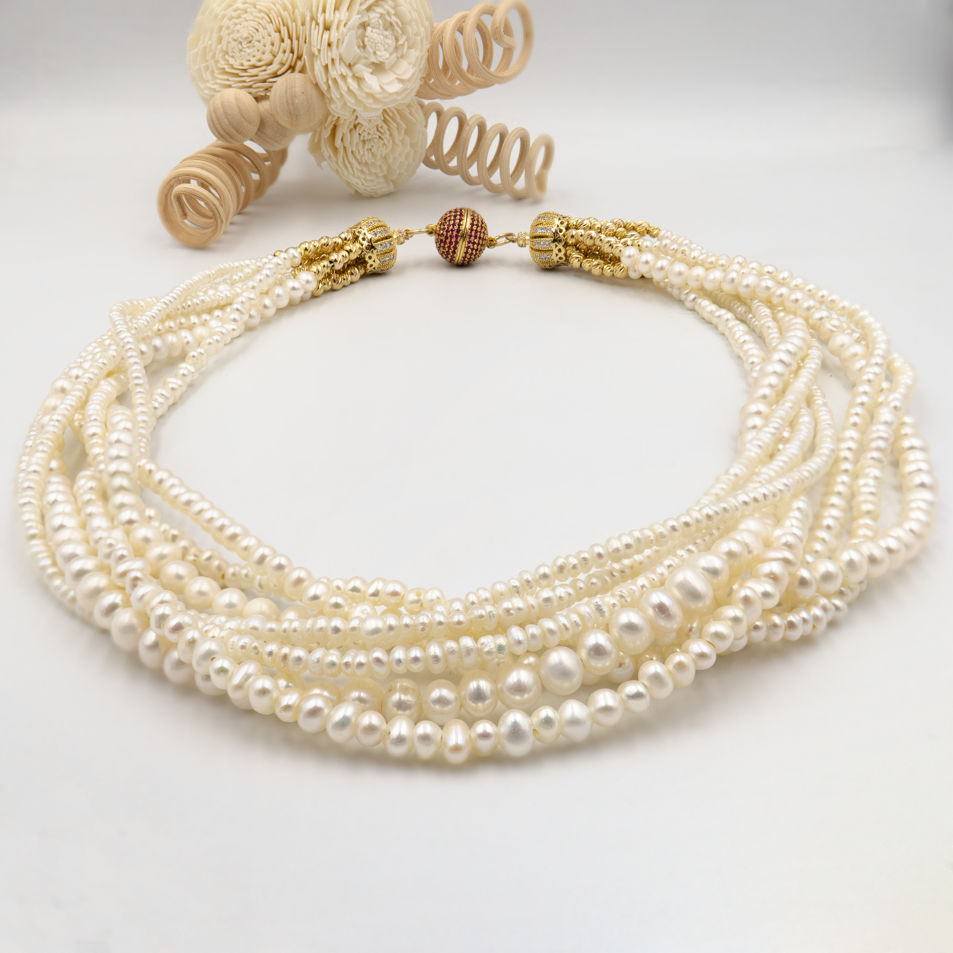 שרשרת שכבות עשירה של פנינים לבנות בשילוב זהב. כל שורת פנינים מוסיפה לתכשיט מימד של תנועה, עומק ויוקרה קלאסית – יחד הן יוצרות נשיות עוצמתית עם איזון עדין. הברק הטבעי של הפנינים משתלב עם האלמנטים המוזהבים לרושם אלגנטי עם טוויסט עכשווי. הסוגר הייחודי, המעוטר באבני קריסטל קטנות בגוון יין עמוק, מהווה מוקד עיצובי שמוסיף עניין ותחושת פאר. שרשרת אידאלית לאירוע חגיגי, חתונה או ערב חשוב – אביזר מרכזי בלוק חגיגי ונשי.