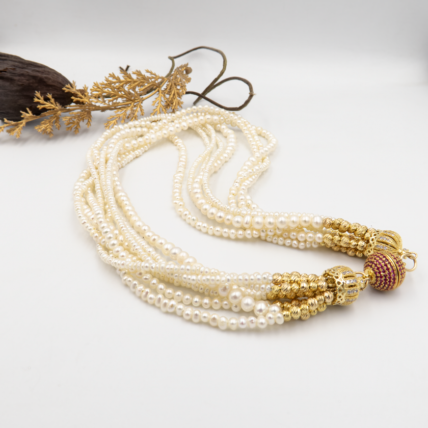 עיצוב אלגנטי עם פנינים טבעיות וסוגר בעיצוב ייחודי. כל שורת פנינים מוסיפה לתכשיט מימד של תנועה, עומק ויוקרה קלאסית – יחד הן יוצרות נשיות עוצמתית עם איזון עדין. הברק הטבעי של הפנינים משתלב עם האלמנטים המוזהבים לרושם אלגנטי עם טוויסט עכשווי. הסוגר הייחודי, המעוטר באבני קריסטל קטנות בגוון יין עמוק, מהווה מוקד עיצובי שמוסיף עניין ותחושת פאר. שרשרת אידאלית לאירוע חגיגי, חתונה או ערב חשוב – אביזר מרכזי בלוק חגיגי ונשי.