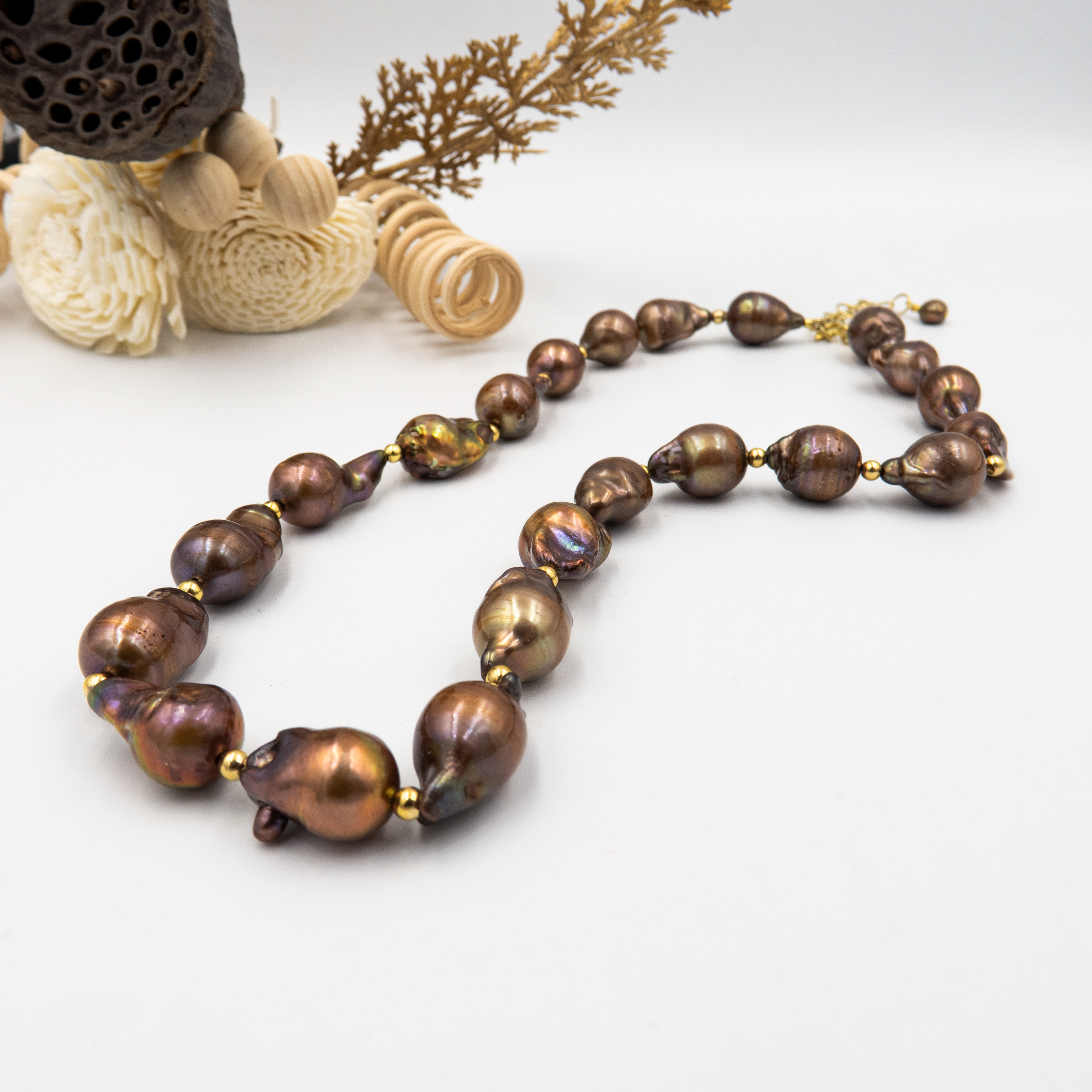 פנינים נדירות בעיצוב שמושך את העין המורכבת מפניני בארוק טבעיות בגוון שוקולד עמוק, עם אביזרים בציפוי זהב שמדגישים את צורתן הבלתי אחידה והמרקם החי של כל פנינה. הברק המטאלי החם של הפנינים משתלב באופן הרמוני עם הנגיעות המוזהבות, ויוצר שילוב של חוזק, נשיות וטבע גולמי. קו עיצובי טבעי עם קריצה לאופנה על־זמנית – אידיאלי לאירוע ערב, להופעה עם אמירה או כמתנה מרשימה לאישה מיוחדת. פניני הבארוק, כל אחת עם אישיות משלה, הופכות את השרשרת הזו לתכשיט שהוא גם אמירה וגם תחושת חיבור אישי.