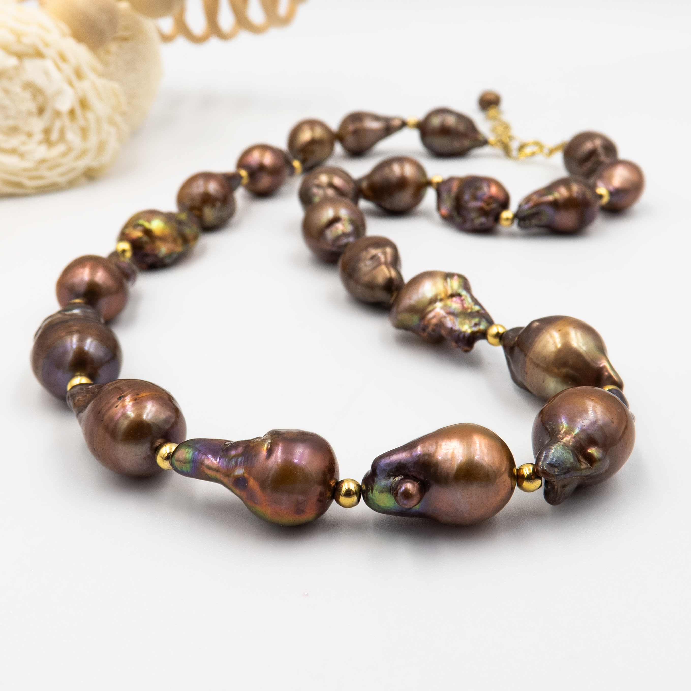 שרשרת יוקרתית בעלת מראה גולמי המורכבת מפניני בארוק טבעיות בגוון שוקולד עמוק, עם אביזרים בציפוי זהב שמדגישים את צורתן הבלתי אחידה והמרקם החי של כל פנינה. הברק המטאלי החם של הפנינים משתלב באופן הרמוני עם הנגיעות המוזהבות, ויוצר רוך פראי בשילוב עם אלגנטיות חמה. קו עיצובי טבעי עם קריצה לאופנה על־זמנית – אידיאלי לאירוע ערב, להופעה עם אמירה או כמתנה מרשימה לאישה מיוחדת. פניני הבארוק, כל אחת עם אישיות משלה, הופכות את השרשרת הזו לבחירה לנשים שמעדיפות ייחוד אמיתי על פני שגרה.