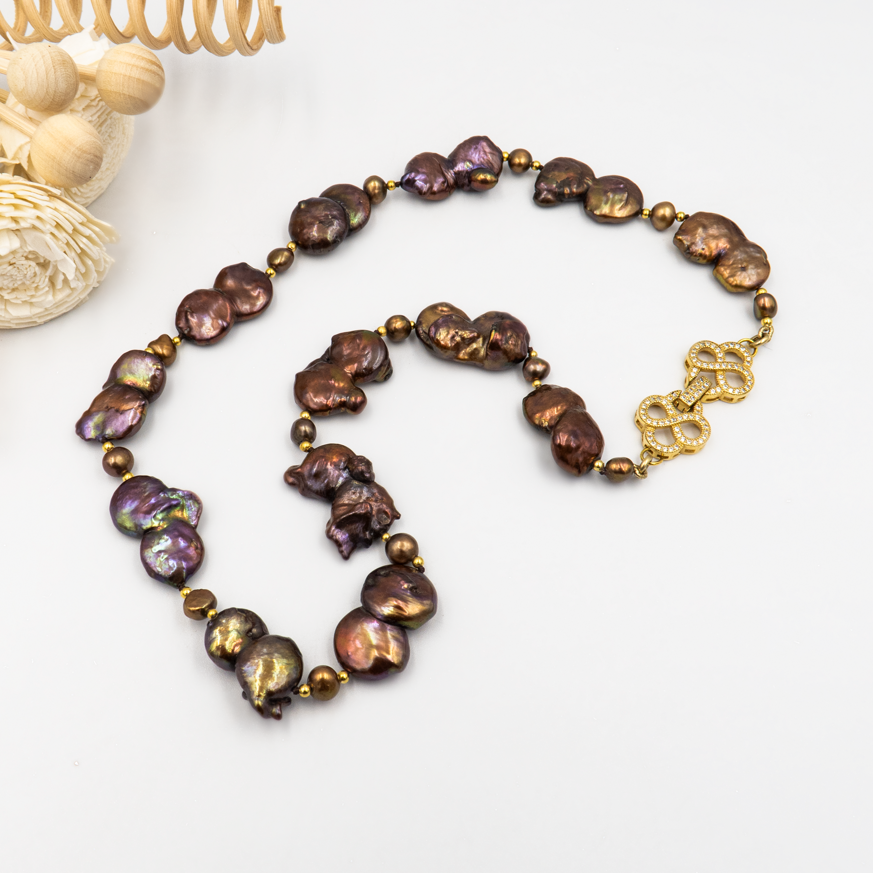 תכשיט בולט עם אופי טבעי המורכבת מפניני בארוק טבעיות בגוון שוקולד עמוק, עם אביזרים בציפוי זהב שמדגישים את צורתן הבלתי אחידה והמרקם החי של כל פנינה. הברק המטאלי החם של הפנינים משתלב באופן הרמוני עם הנגיעות המוזהבות, ויוצר תחושה של חומר חי ונושם. שילוב קלאסי ונועז כאחד – אידיאלי לאירוע ערב, להופעה עם אמירה או כמתנה מרשימה לאישה מיוחדת. פניני הבארוק, כל אחת עם אישיות משלה, הופכות את השרשרת הזו לשרשרת שלא דומה לשום דבר אחר – טבעית, אותנטית ומרשימה.