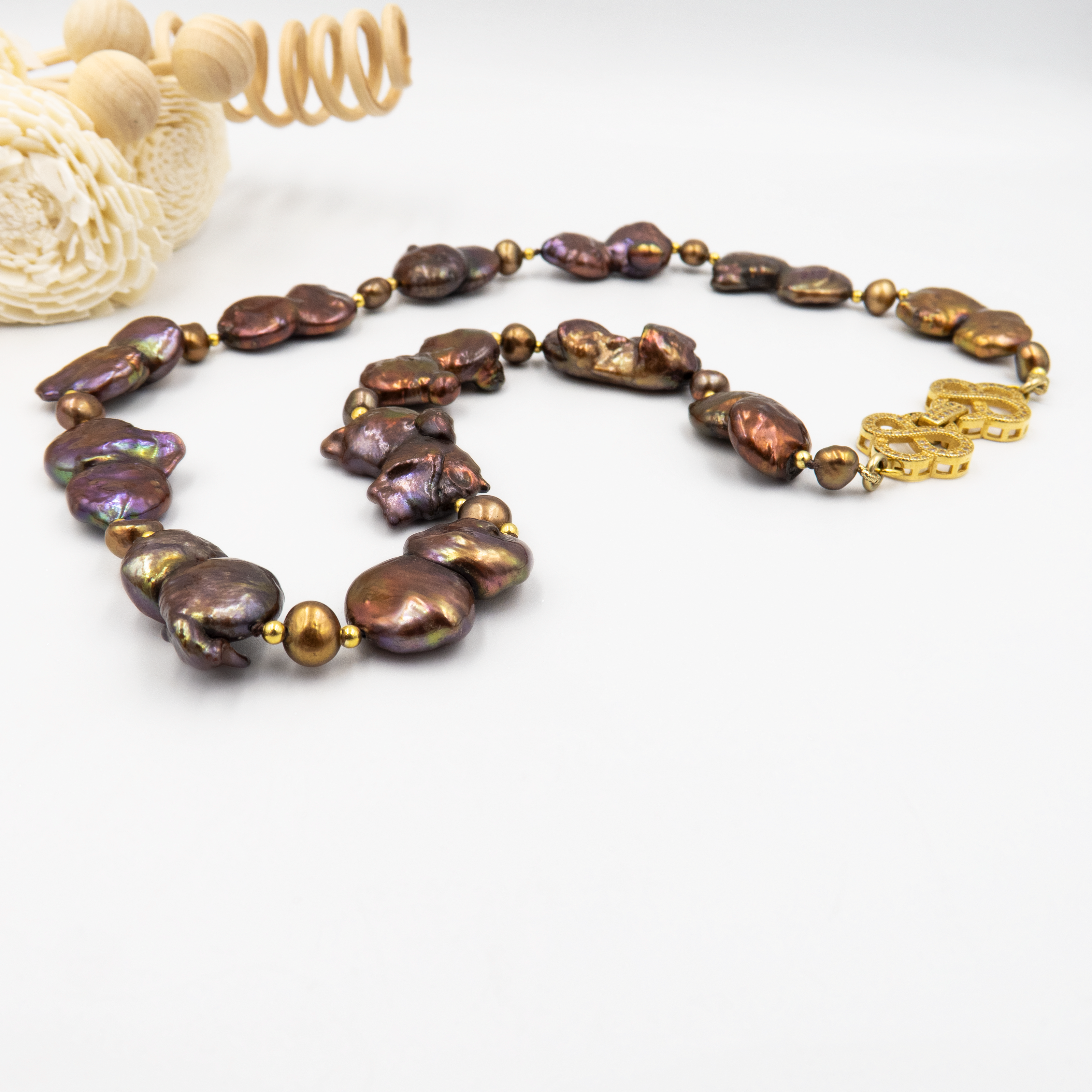 שרשרת נדירה שמדברת בעד עצמה המורכבת מפניני בארוק טבעיות בגוון שוקולד עמוק, עם אביזרים בציפוי זהב שמדגישים את צורתן הבלתי אחידה והמרקם החי של כל פנינה. הברק המטאלי החם של הפנינים משתלב באופן הרמוני עם הנגיעות המוזהבות, ויוצר תחושה של חומר חי ונושם. שילוב קלאסי ונועז כאחד – אידיאלי לאירוע ערב, להופעה עם אמירה או כמתנה מרשימה לאישה מיוחדת. פניני הבארוק, כל אחת עם אישיות משלה, הופכות את השרשרת הזו למבט אחד מספיק כדי להבין – זה תכשיט עם נוכחות.